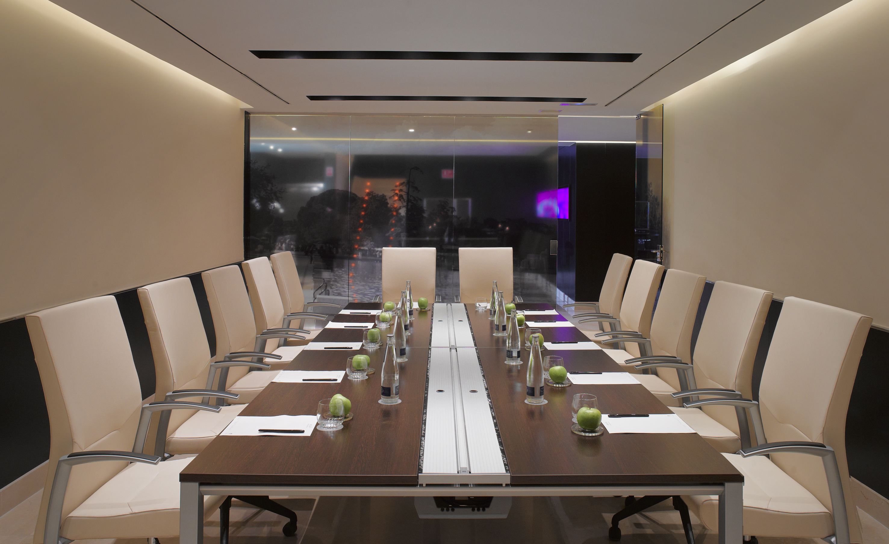 Modern conference room with dark wood table, beige chairs, water, and apples.