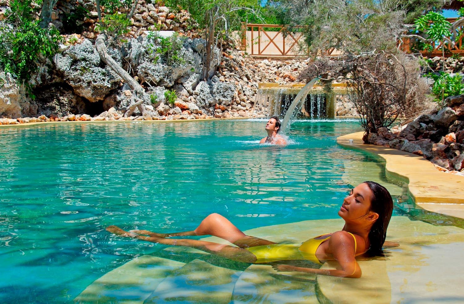 a woman in a yellow swimsuit in a pool with a man in the background