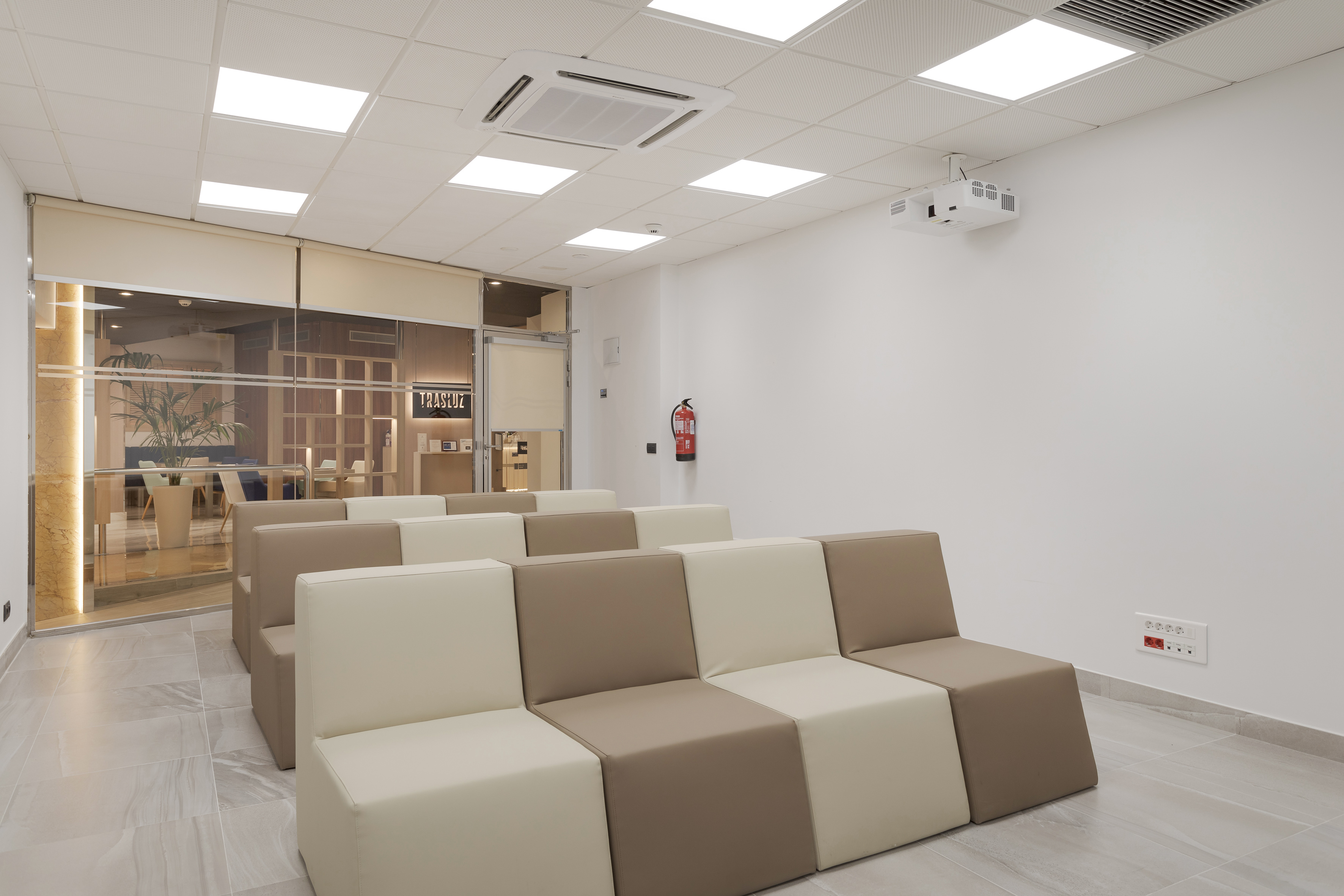 Modern meeting room with beige modular seating, projector, and bright lighting.