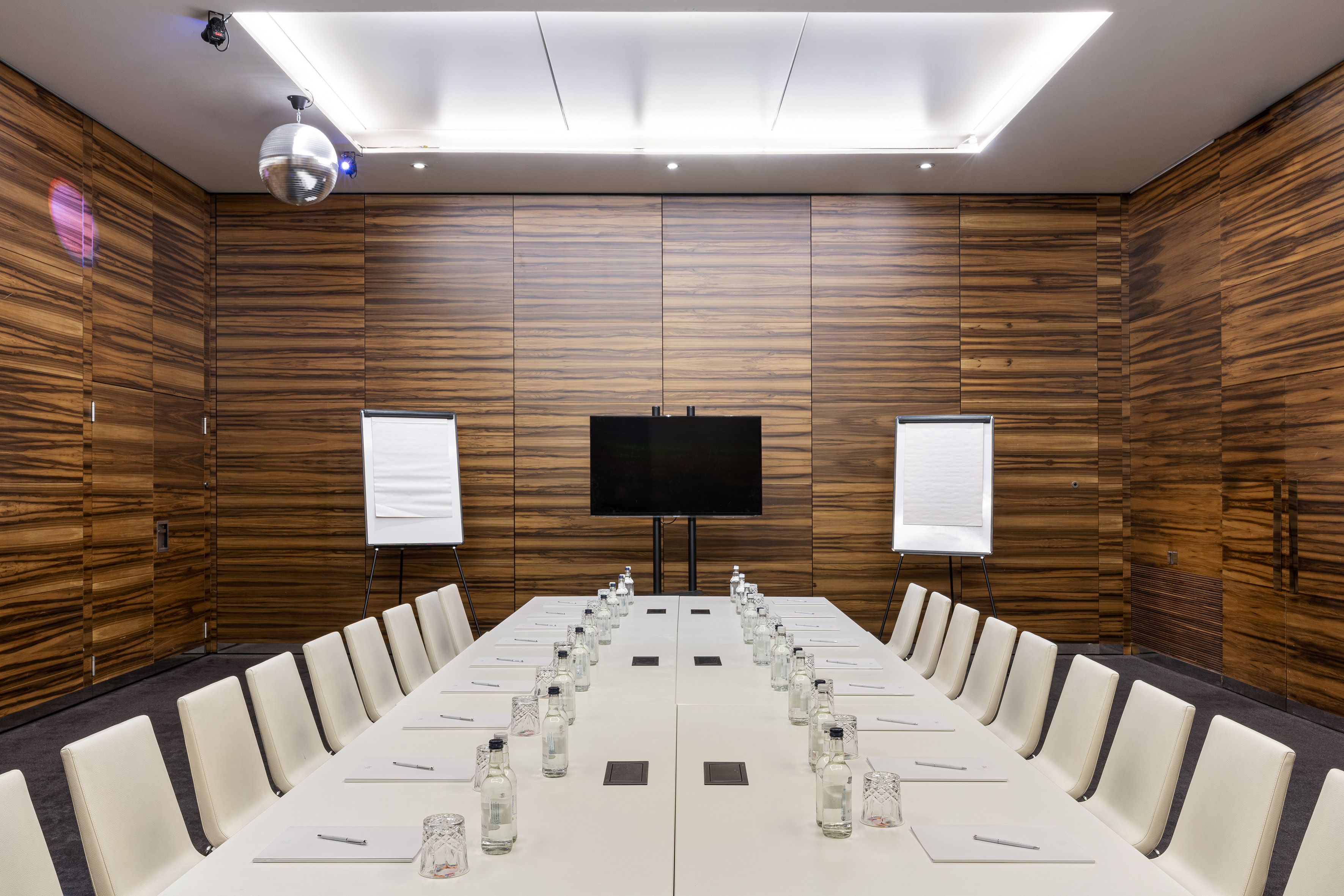 Executive conference room with wood paneling, large screen, and white table.