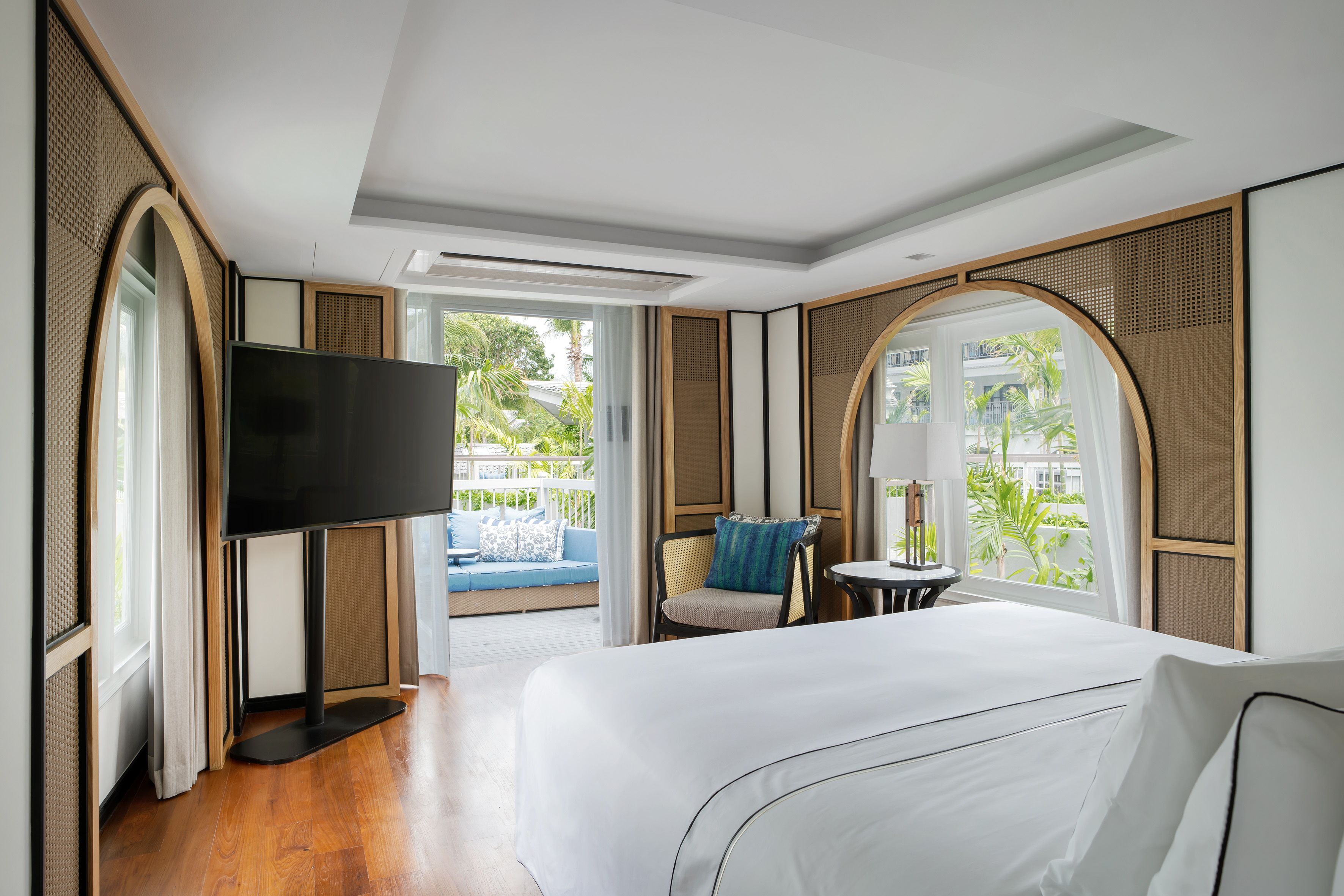 Modern hotel bedroom with king bed, TV, balcony, and tropical garden view.