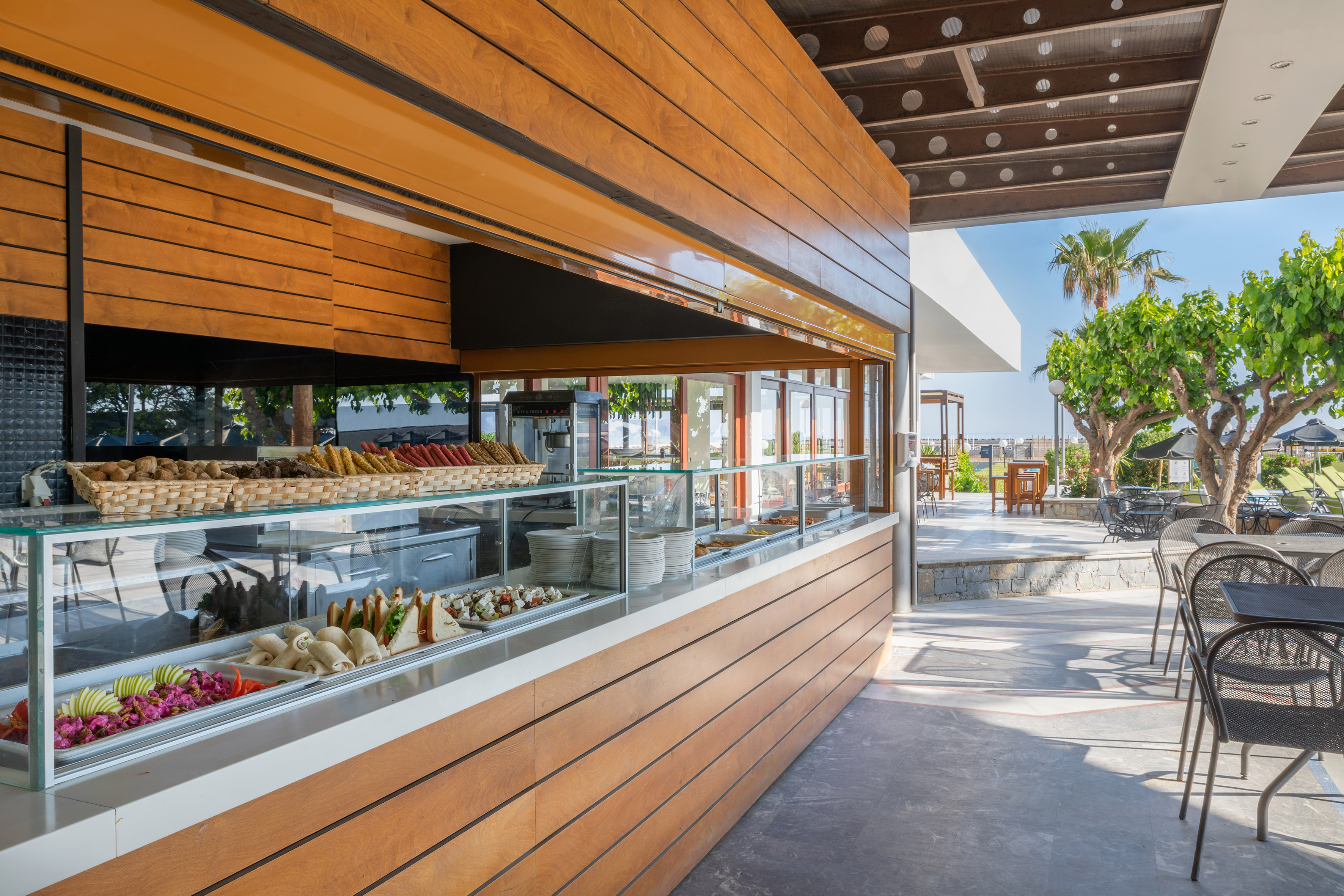 Outdoor resort buffet with food displays, wooden counter, and sunny patio.