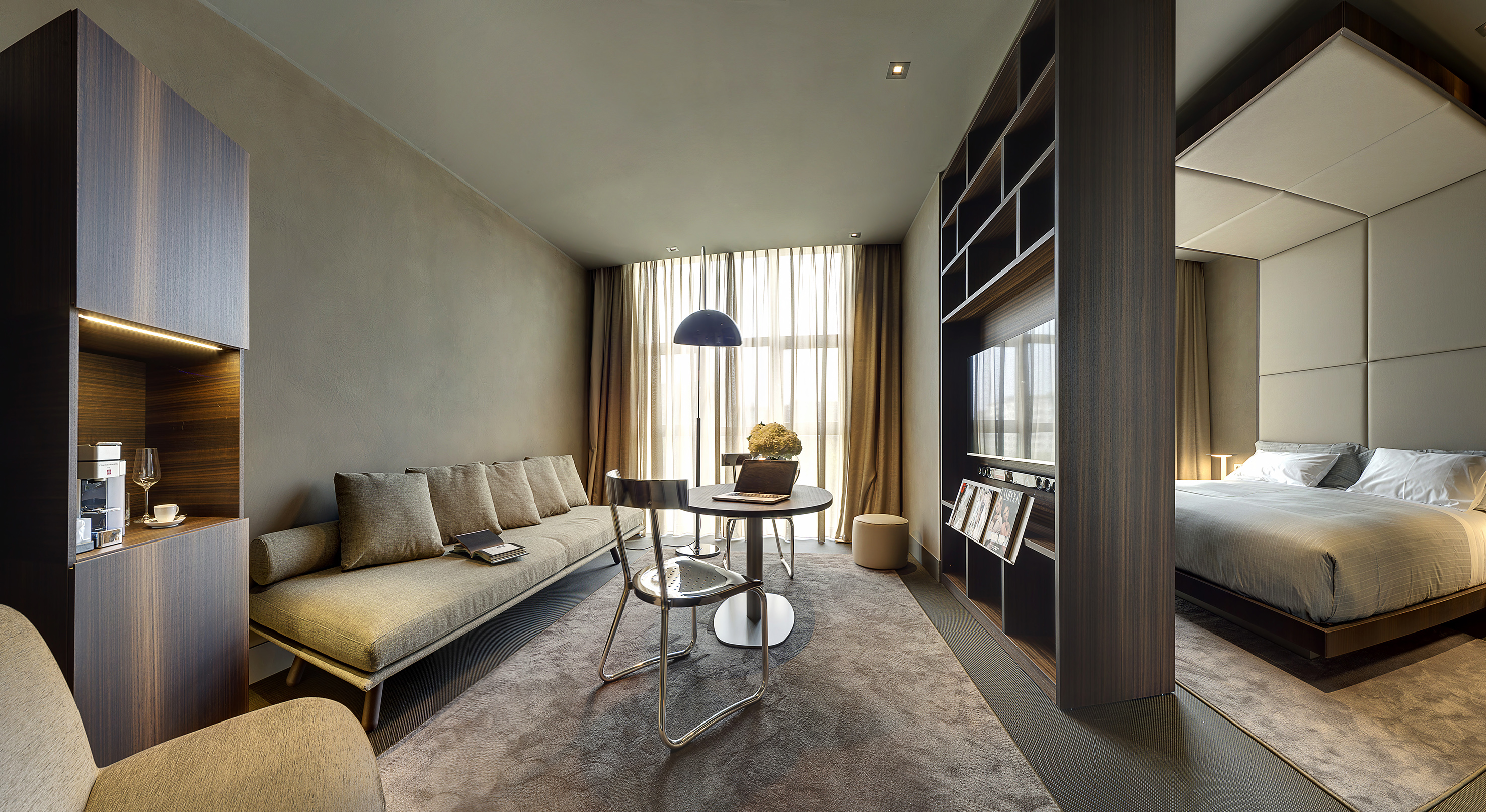 Modern hotel suite with living area, sofa, work desk, and cozy bedroom.