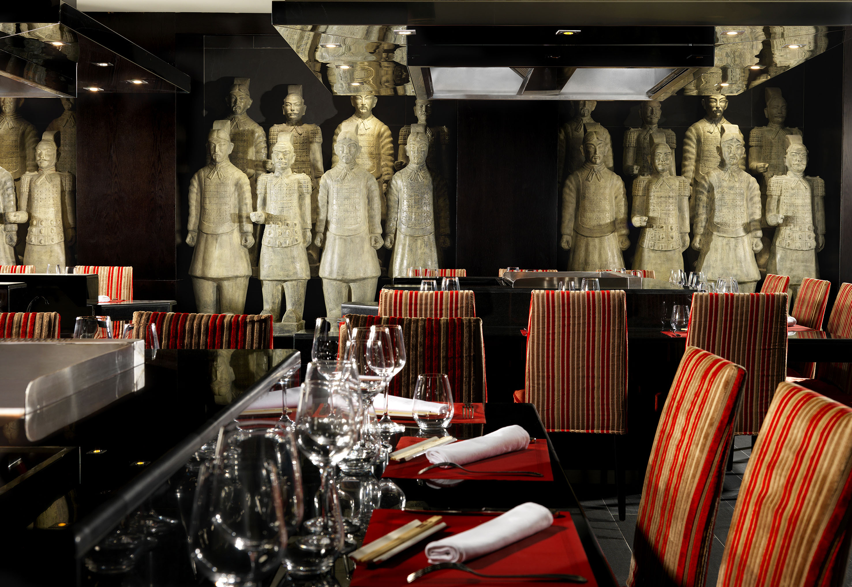 Chinese restaurant dining area with terracotta warriors, reflective tables, red chairs.