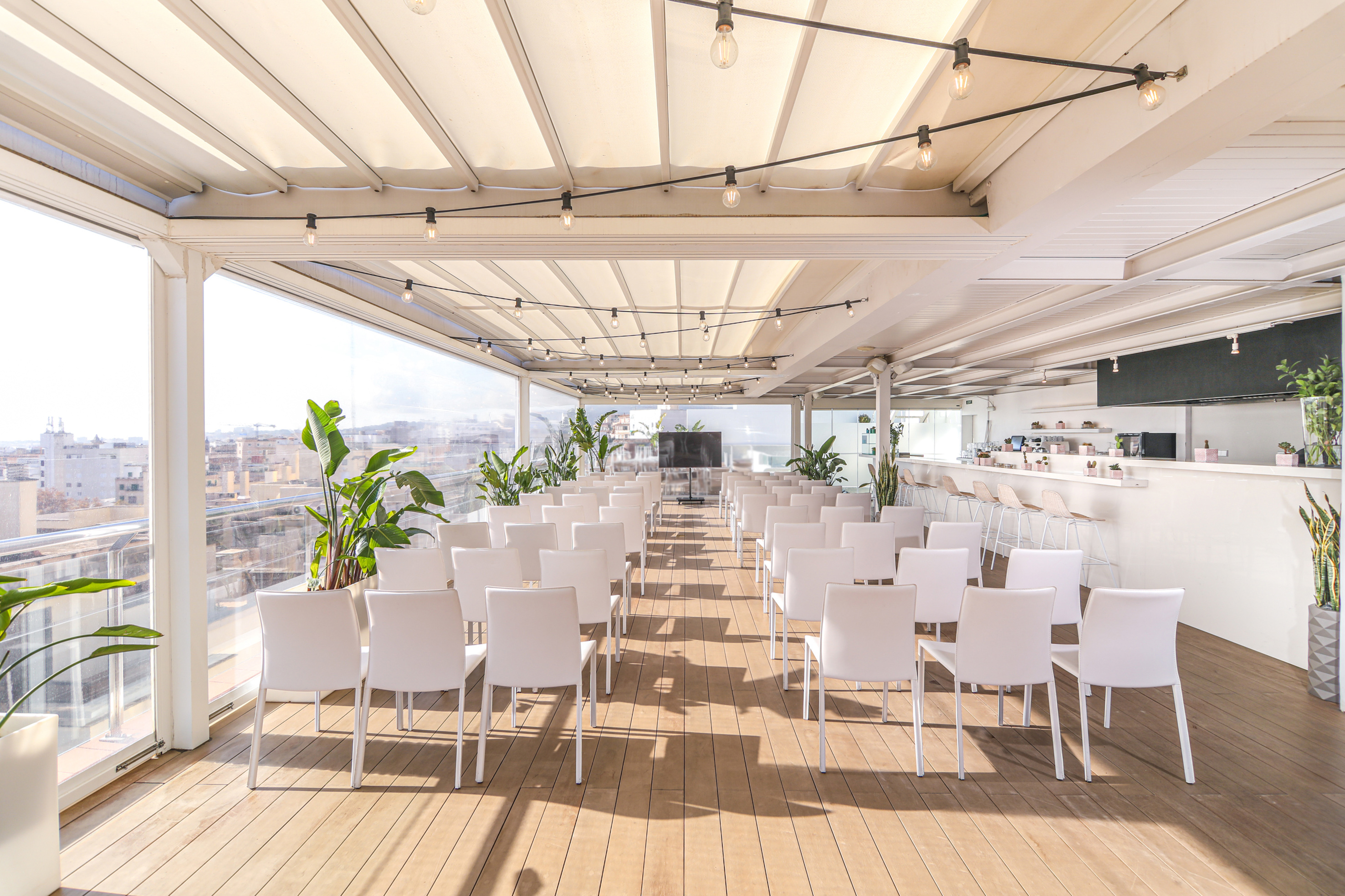 Rooftop conference terrace with white chairs, bar, and city skyline view.