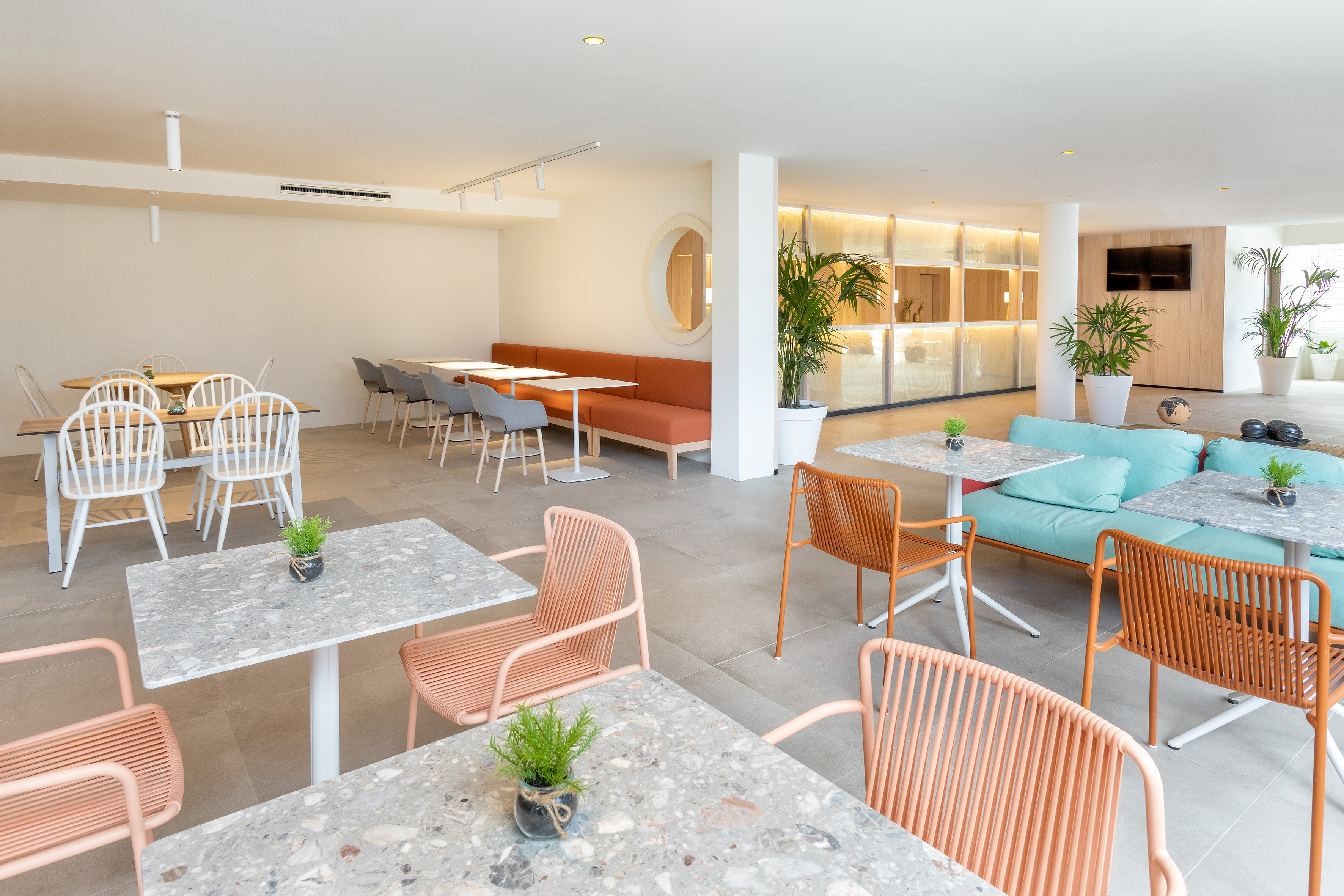 Bright, modern cafe interior with diverse seating, terrazzo tables, and plants.