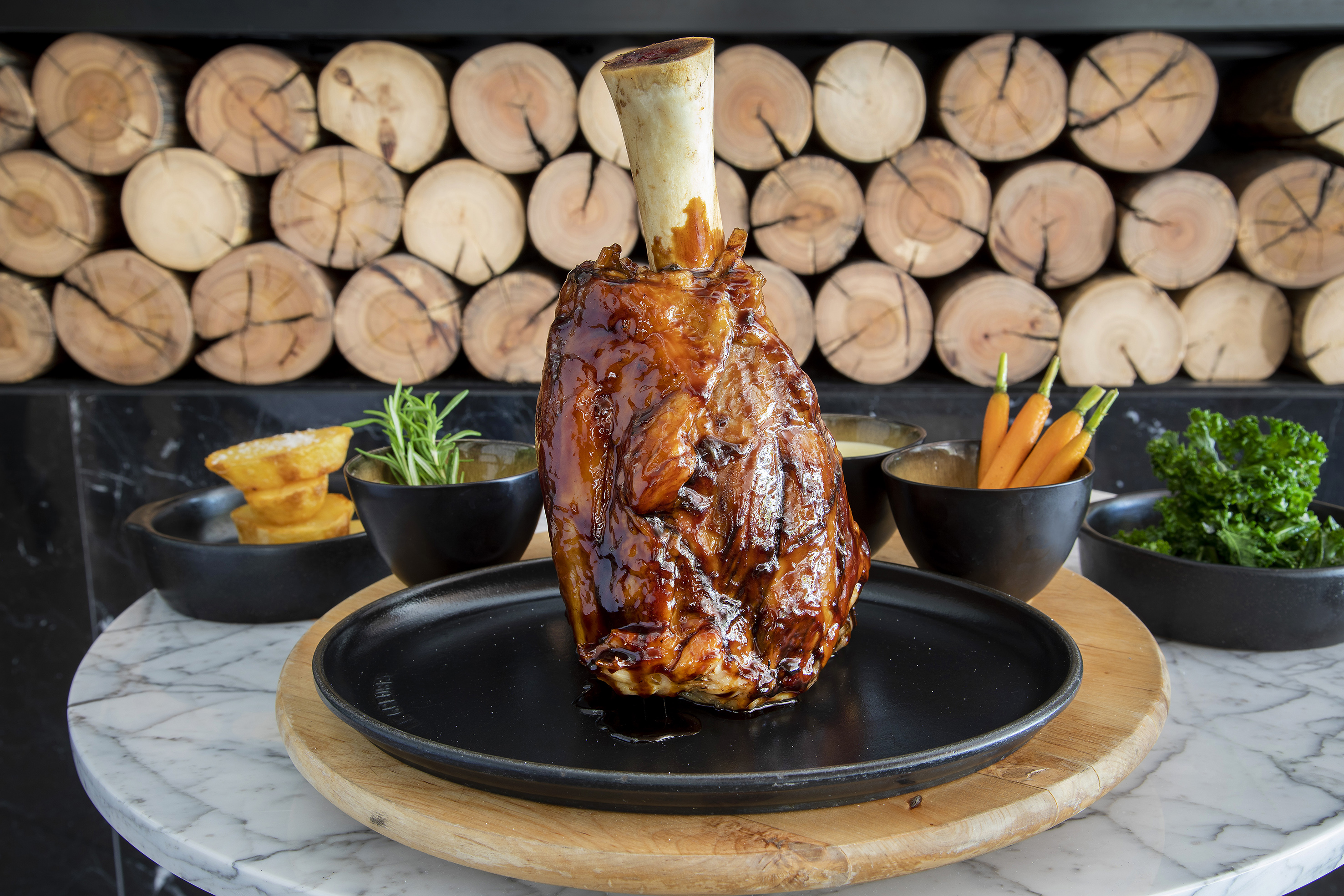 Glazed lamb shank, roasted potatoes, baby carrots, and rosemary, rustic setting.