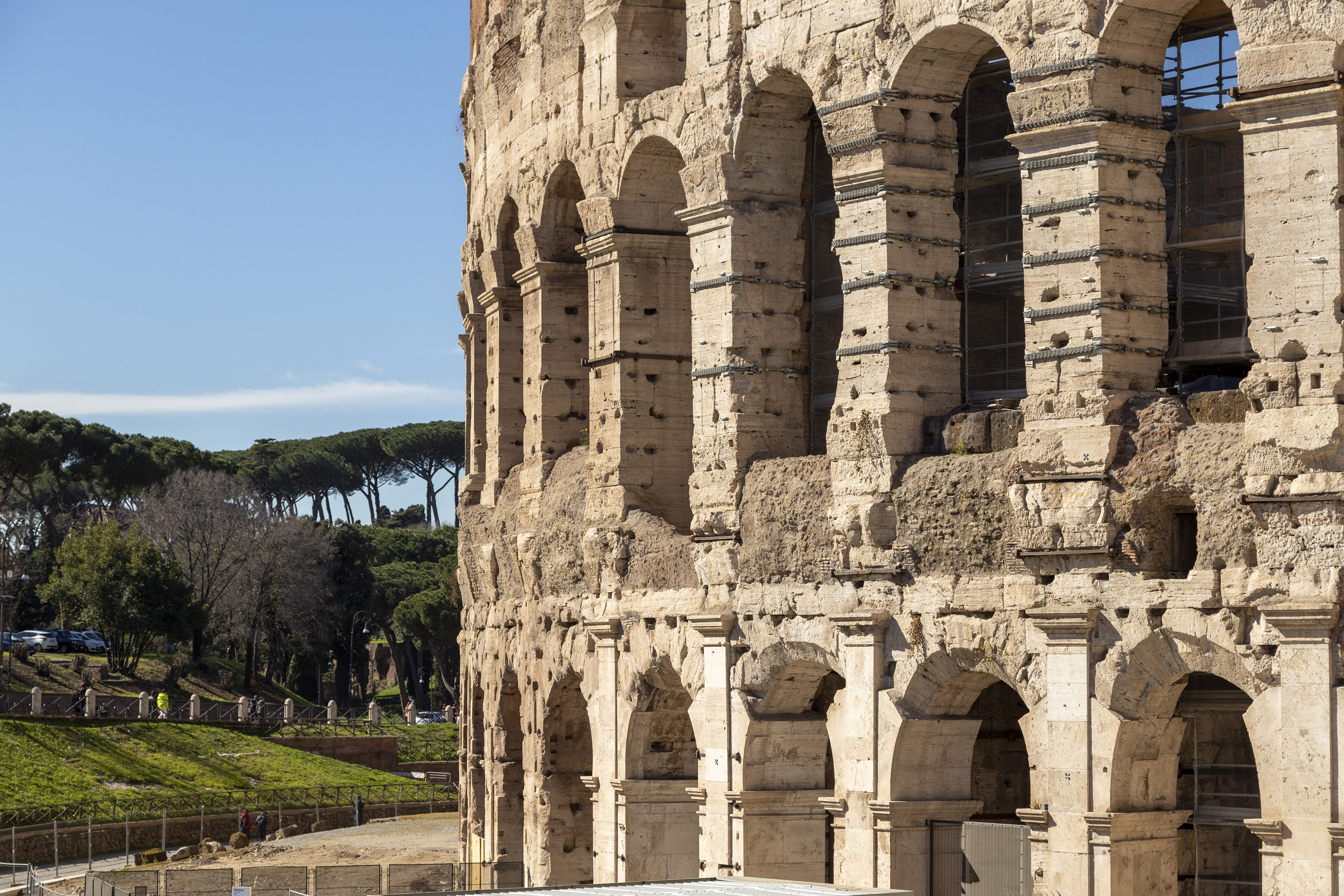 Weathered stone arches of the Colosseum in Rome under a clear blue sky.
