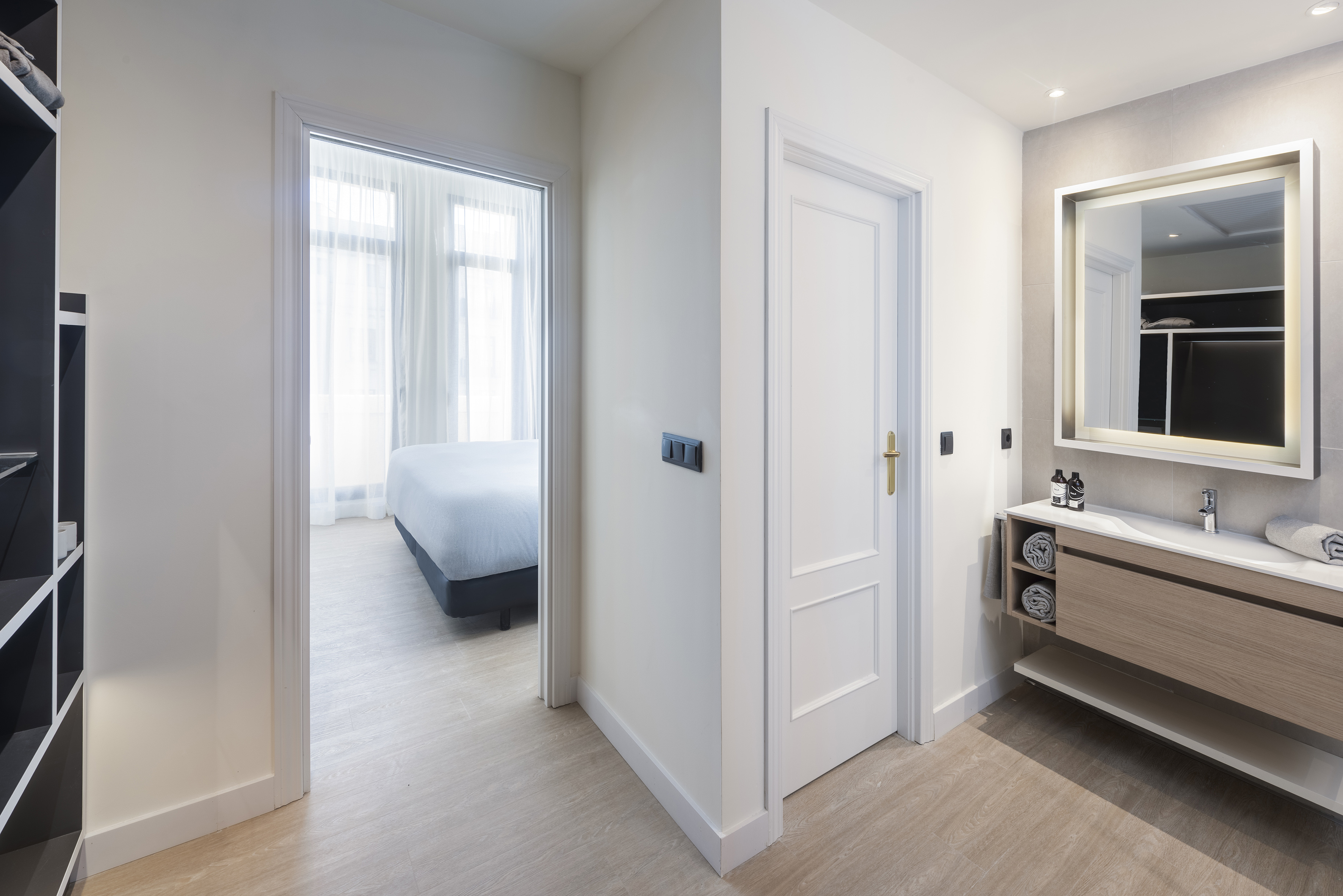 Modern hotel suite featuring bathroom vanity, illuminated mirror, and bedroom.