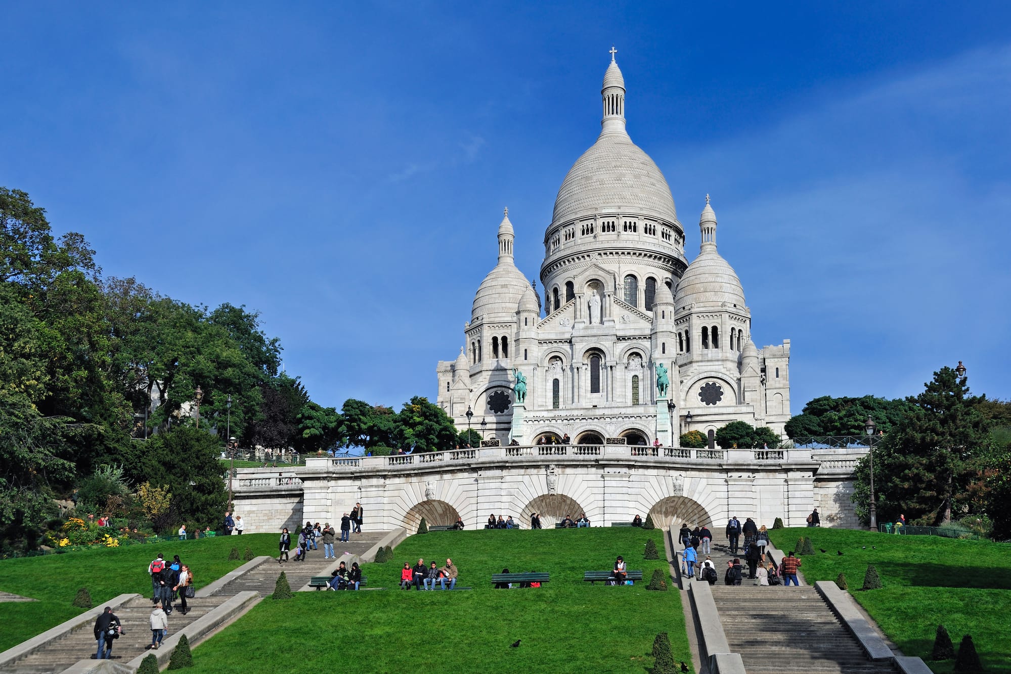 a large white building with a dome and a steeple and people walking on the grass with Sacré-Cœur, Paris in the background