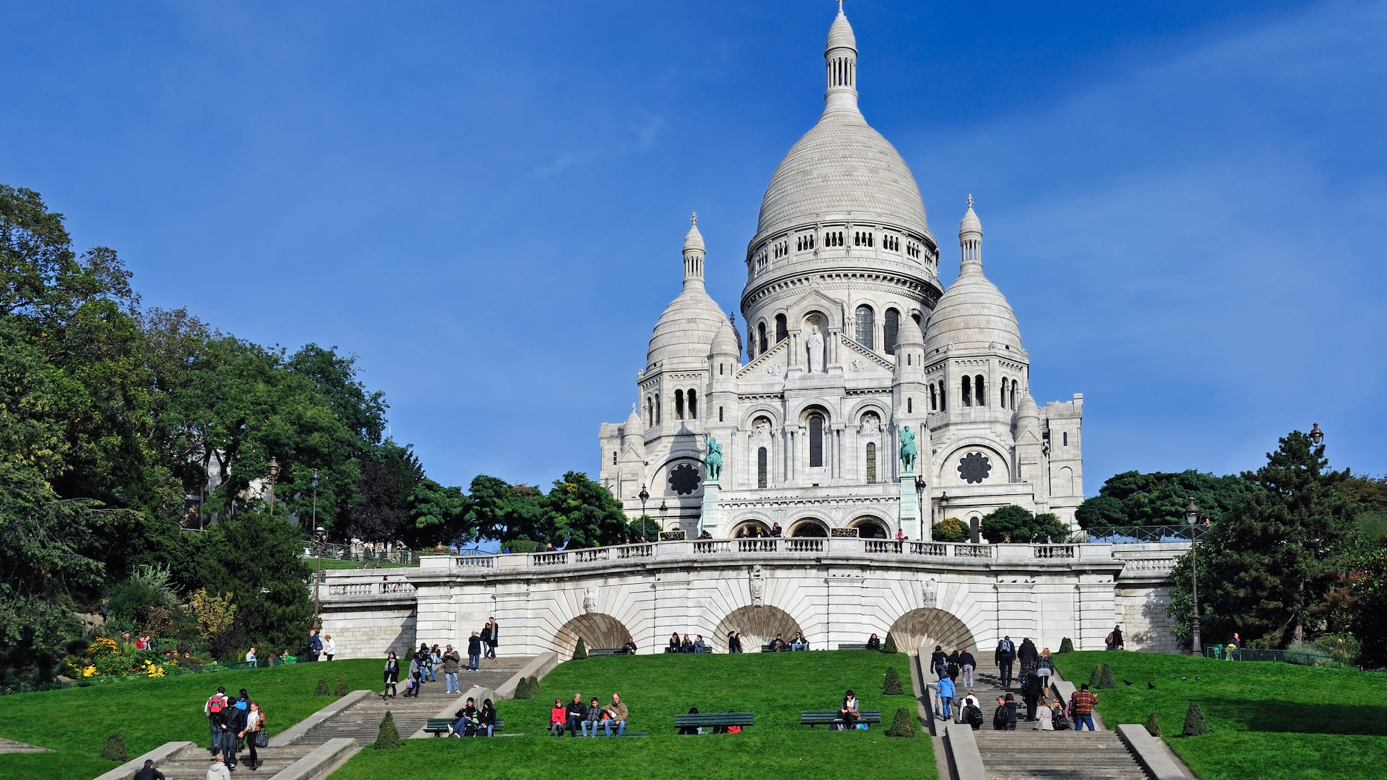 a large white building with a dome and a steeple and people walking on the grass with Sacré-Cœur, Paris in the background