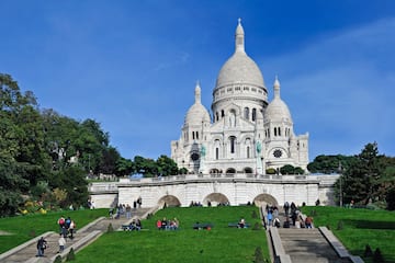 a large white building with a dome and a steeple and people walking on the grass with Sacré-Cœur, Paris in the background