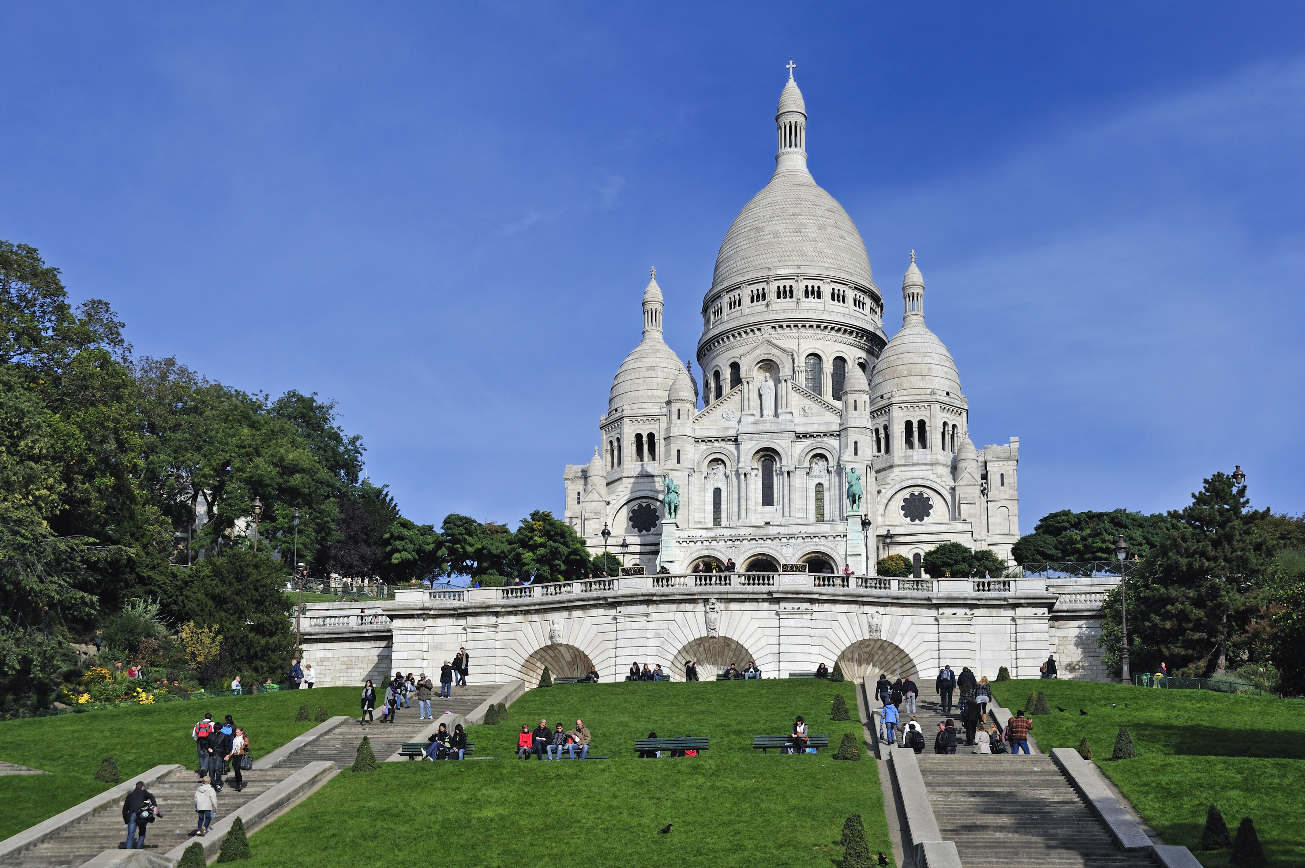 a large white building with a dome and a steeple and people walking on the grass with Sacré-Cœur, Paris in the background