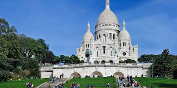 a large white building with a dome and a steeple and people walking on the grass with Sacré-Cœur, Paris in the background