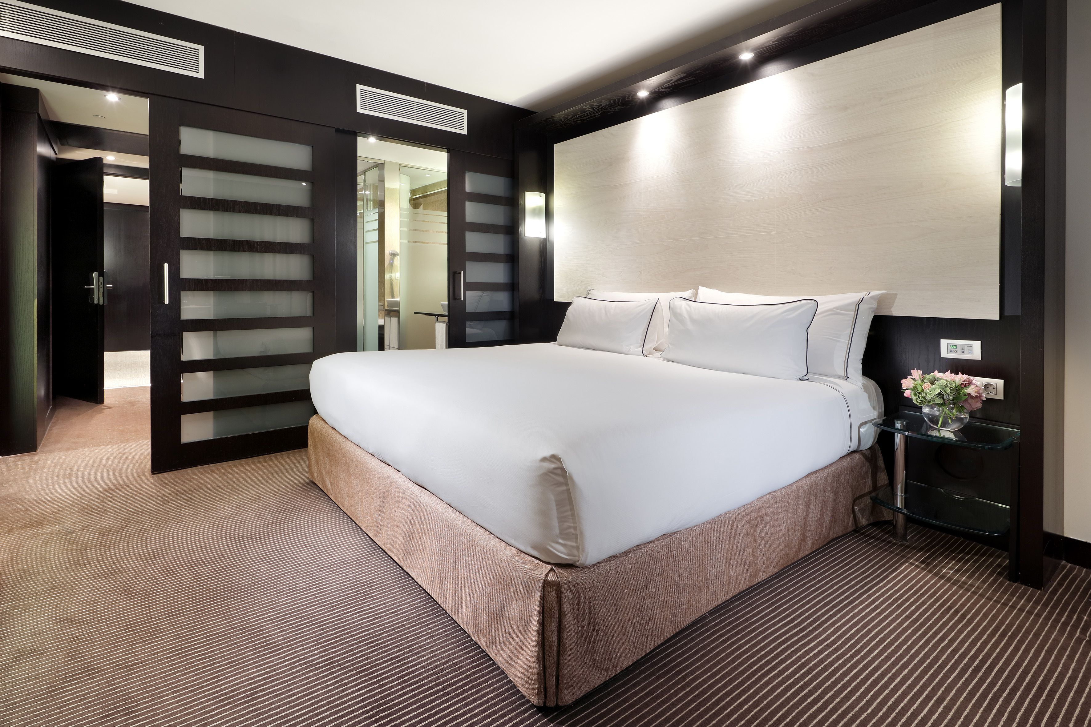 Luxury hotel bedroom with king bed, modern dark wood, frosted sliding doors.