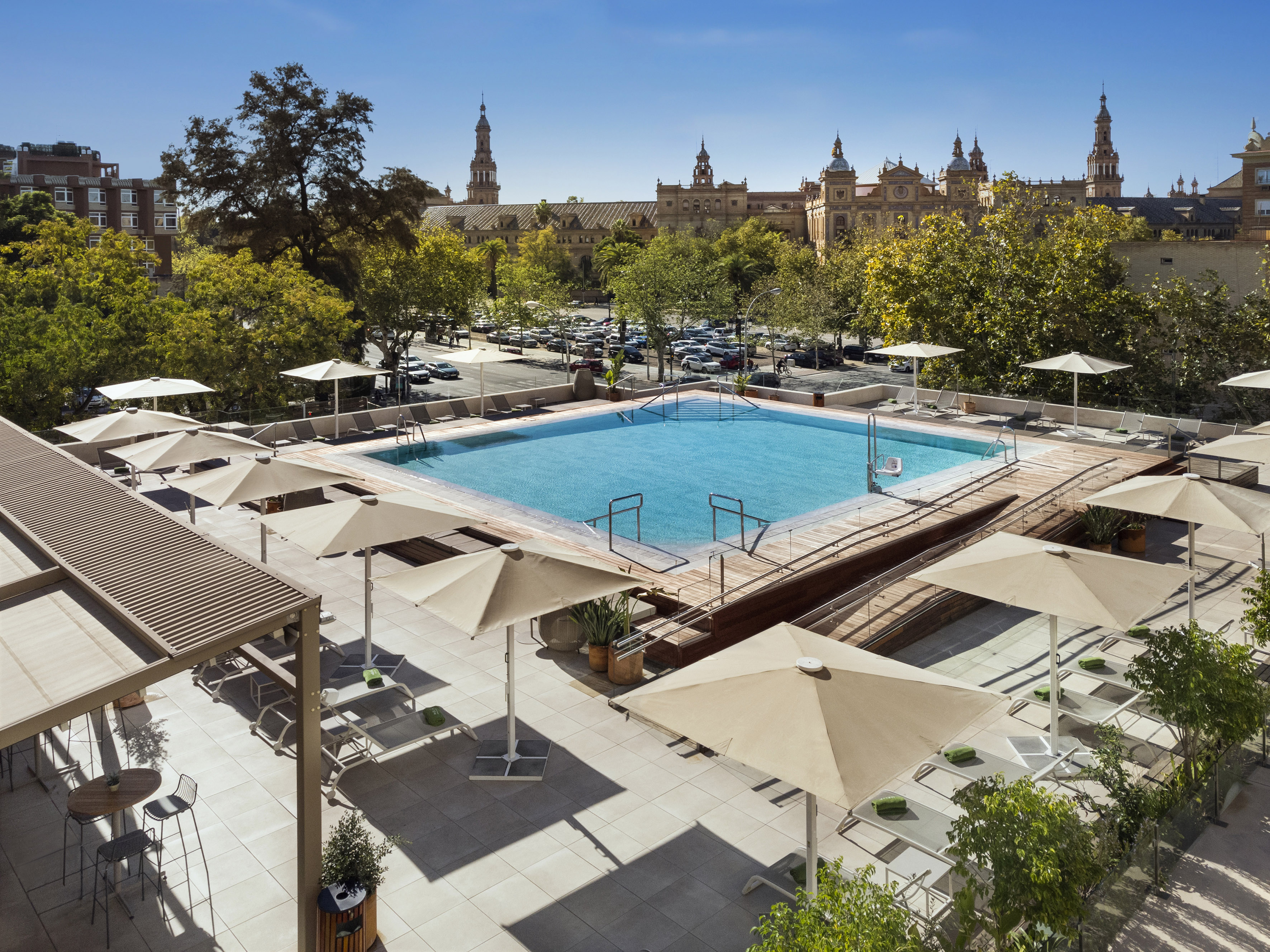 Rooftop pool and deck with umbrellas, overlooking Seville's Plaza de España.