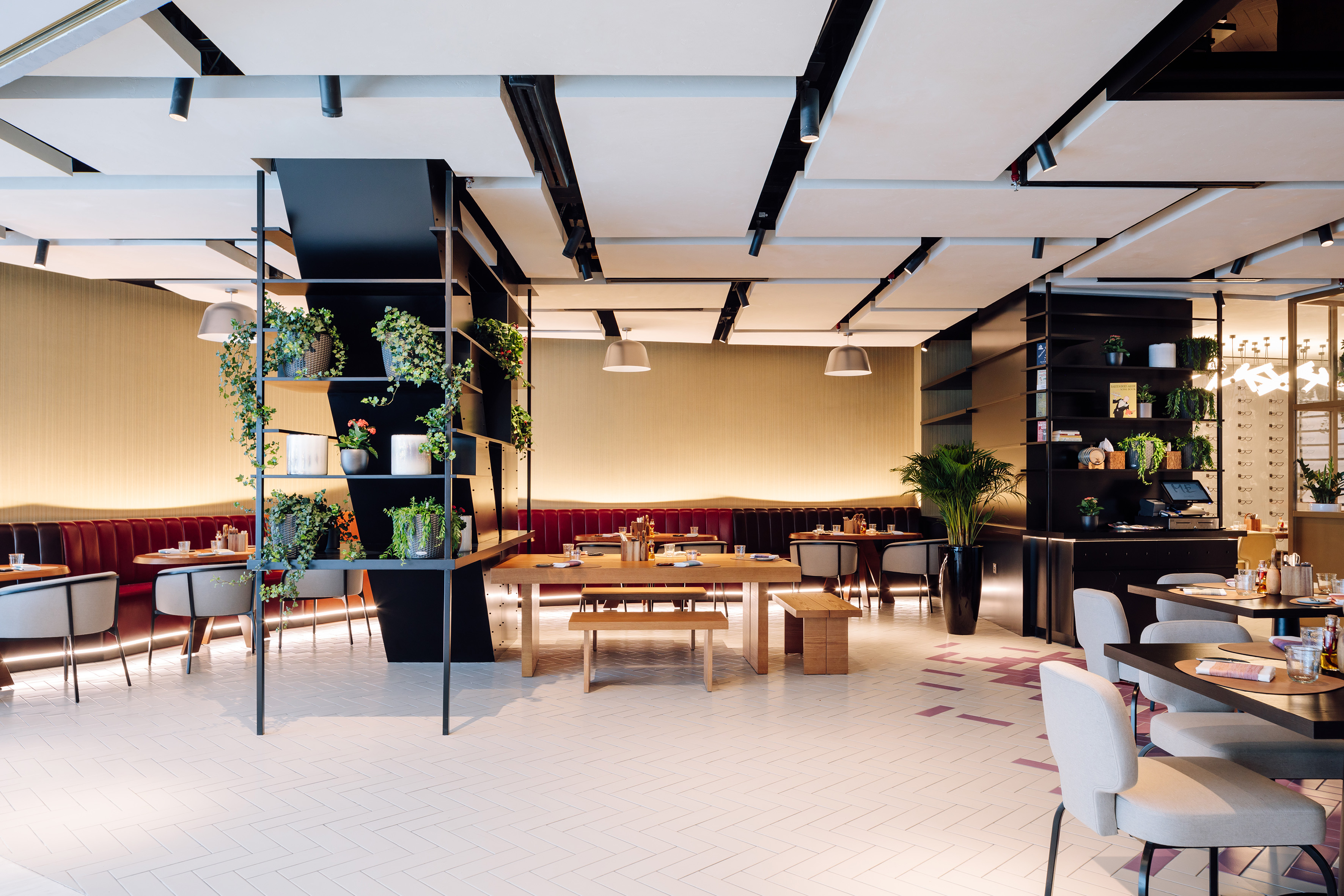 Modern restaurant interior with plants, booths, tables, and stylish lighting.