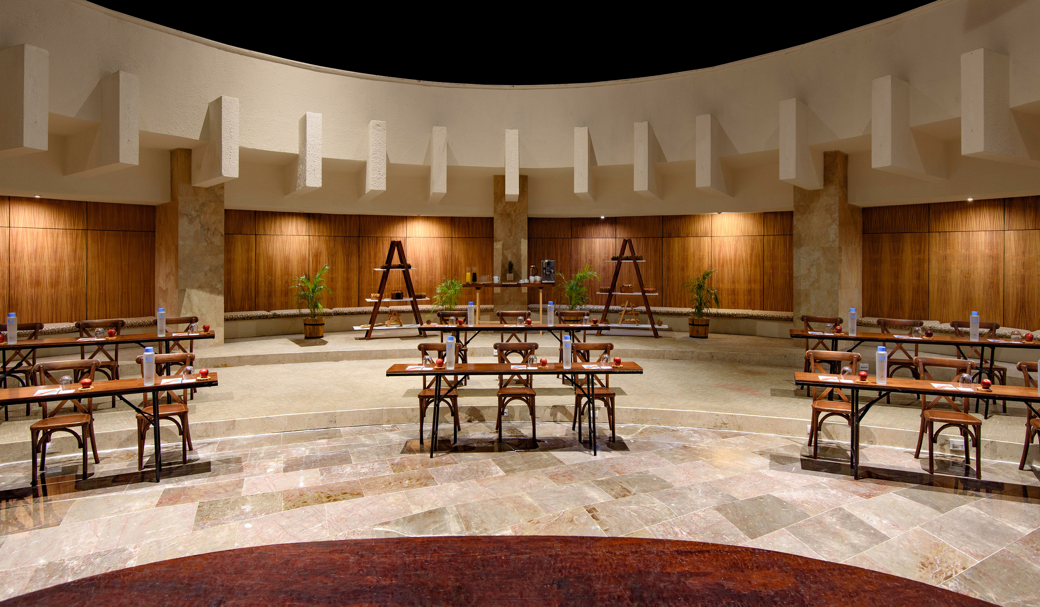 Tiered conference room, wooden tables and chairs, curved buffet setup for events.