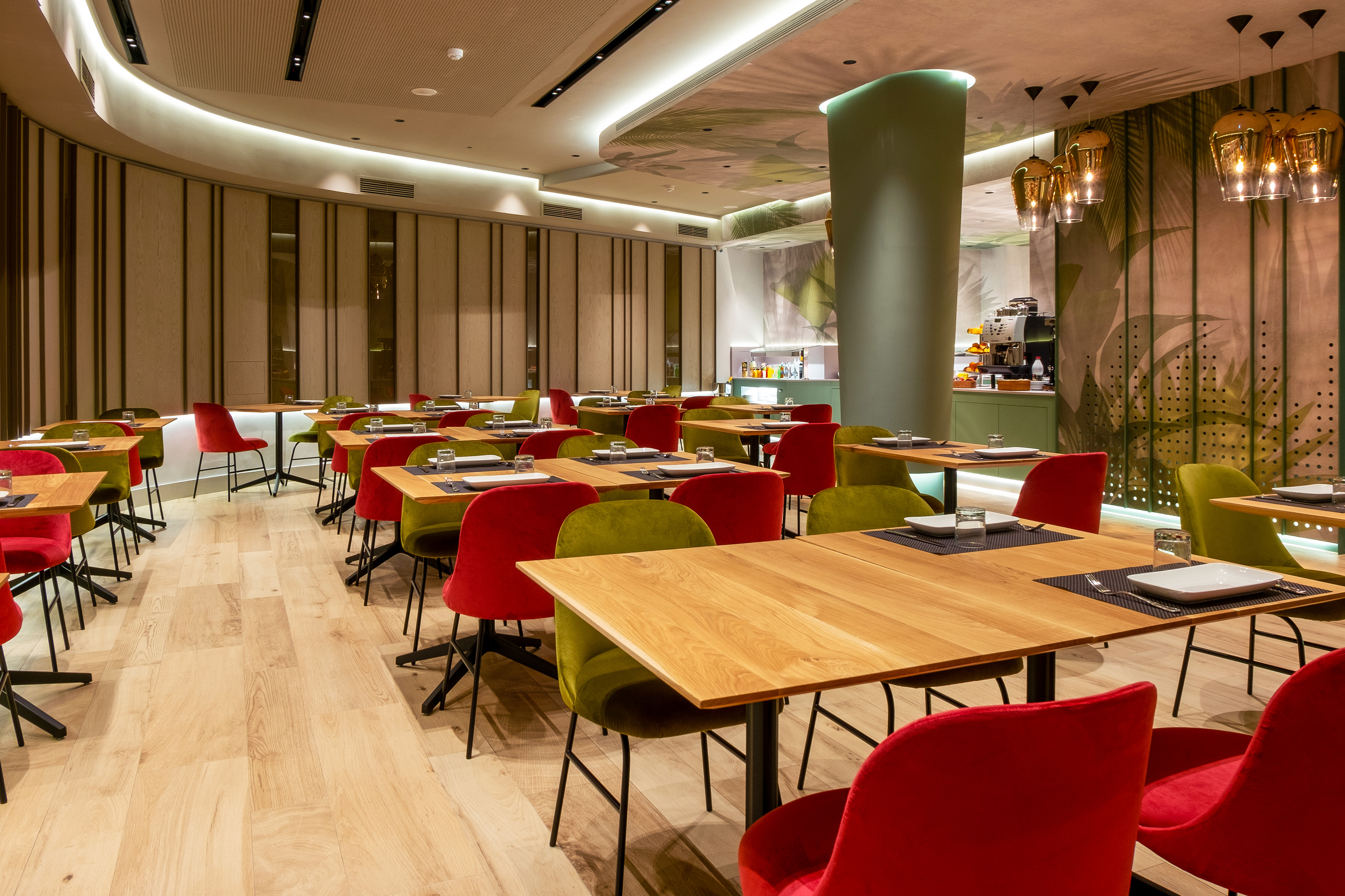 Modern restaurant interior with wooden tables, red & green chairs, botanical decor.