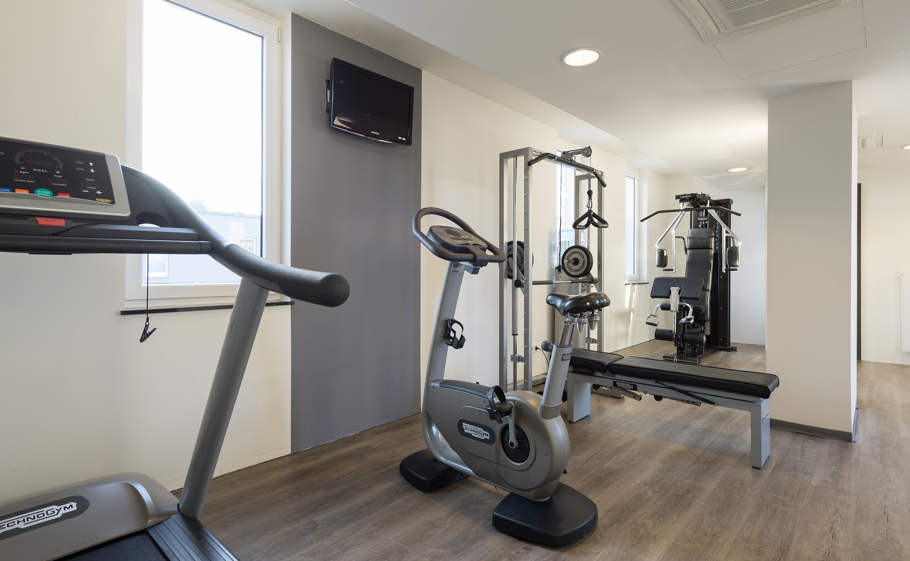 Modern gym with Technogym treadmill, exercise bike, and multi-gym equipment.
