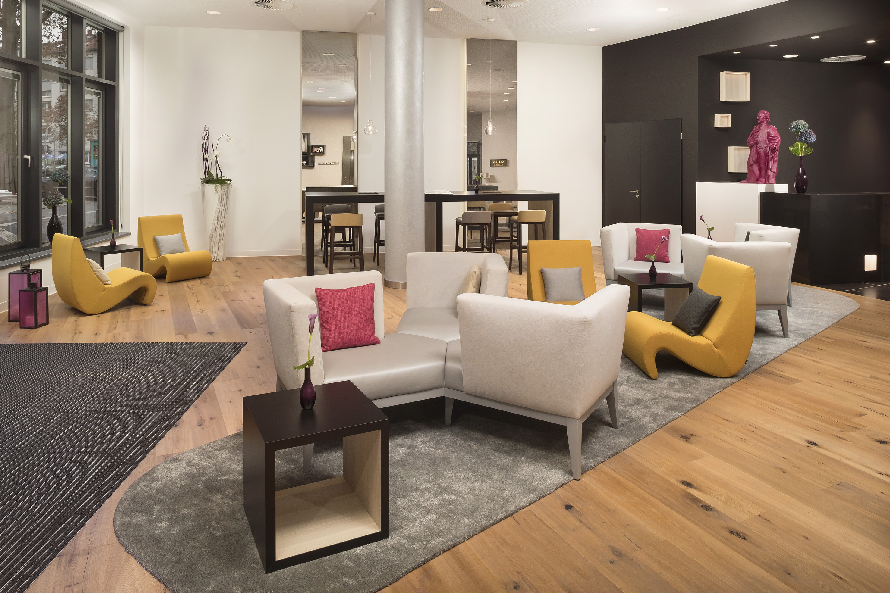 Modern hotel lounge with yellow & grey seating, light wood floor, dark reception.