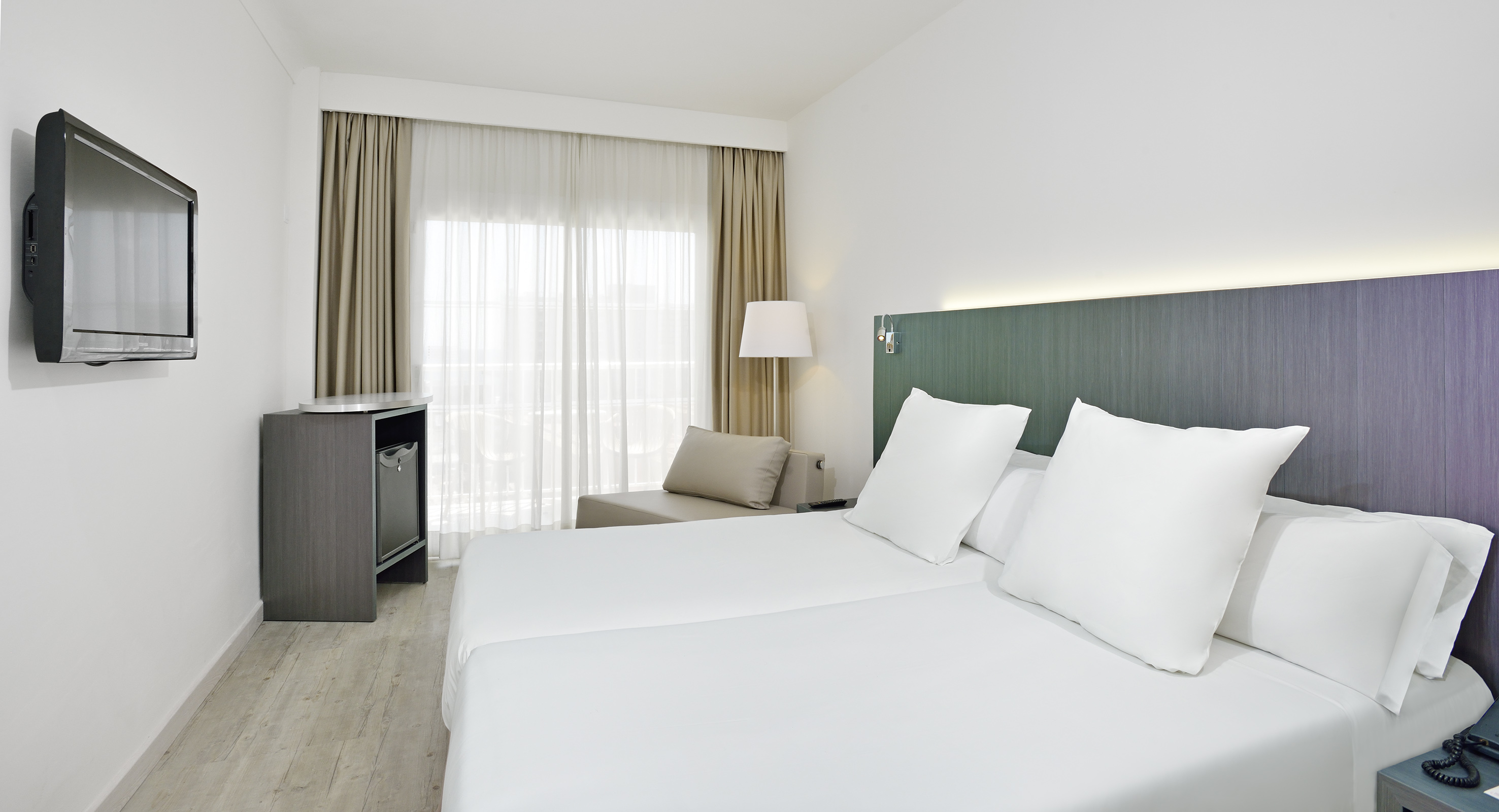 Modern hotel room with twin beds, white linens, wall TV, and large window.