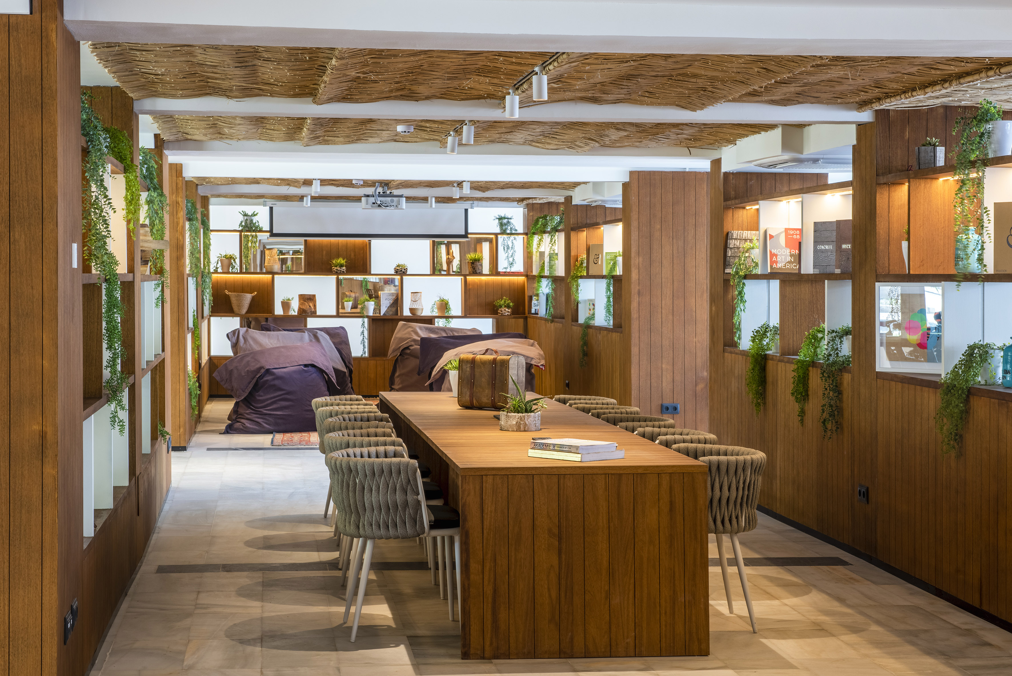 Biophilic co-working room with wood table, shelves, plants, and lounge area.