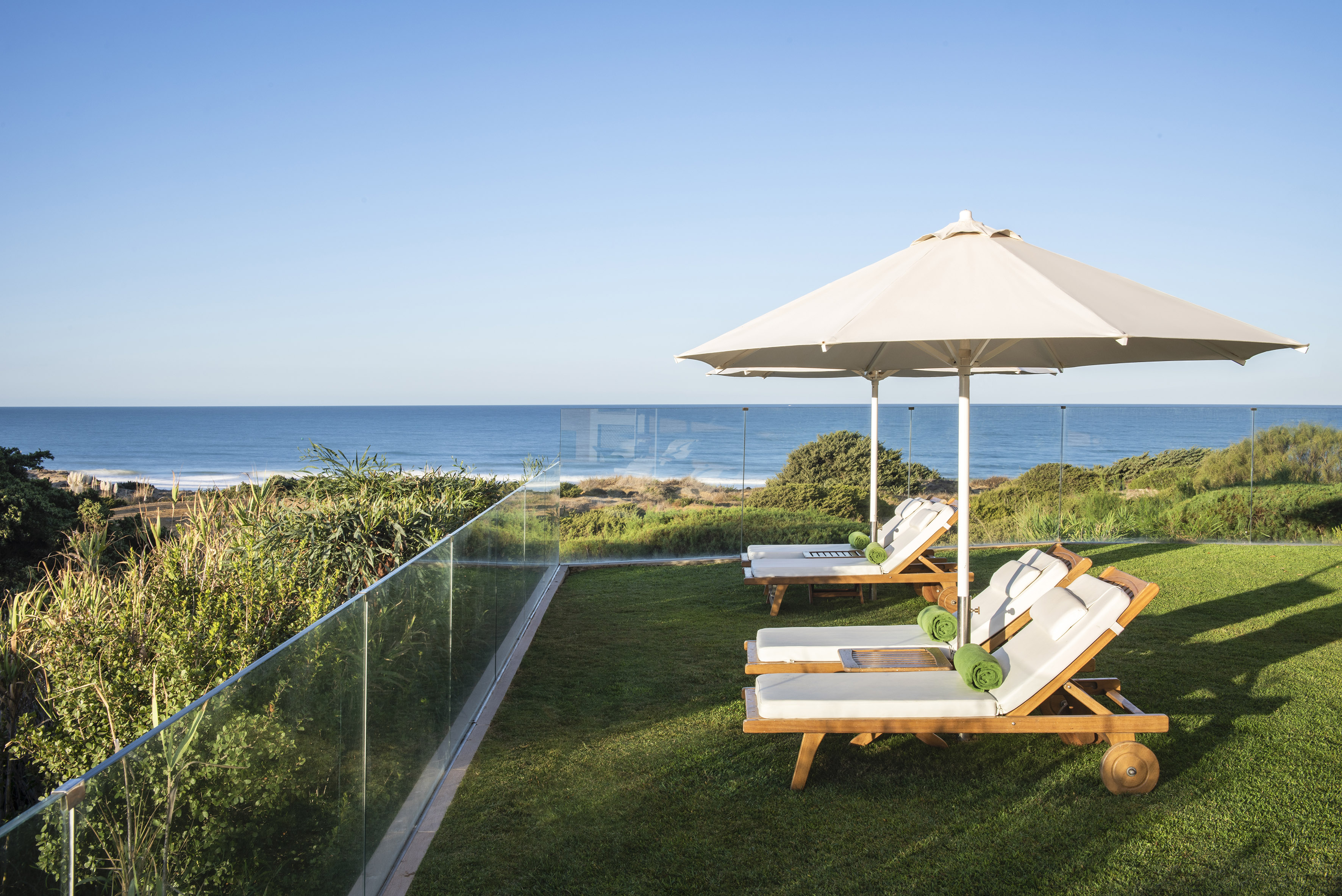 Luxury oceanfront terrace with lounge chairs, umbrella, and glass railing.