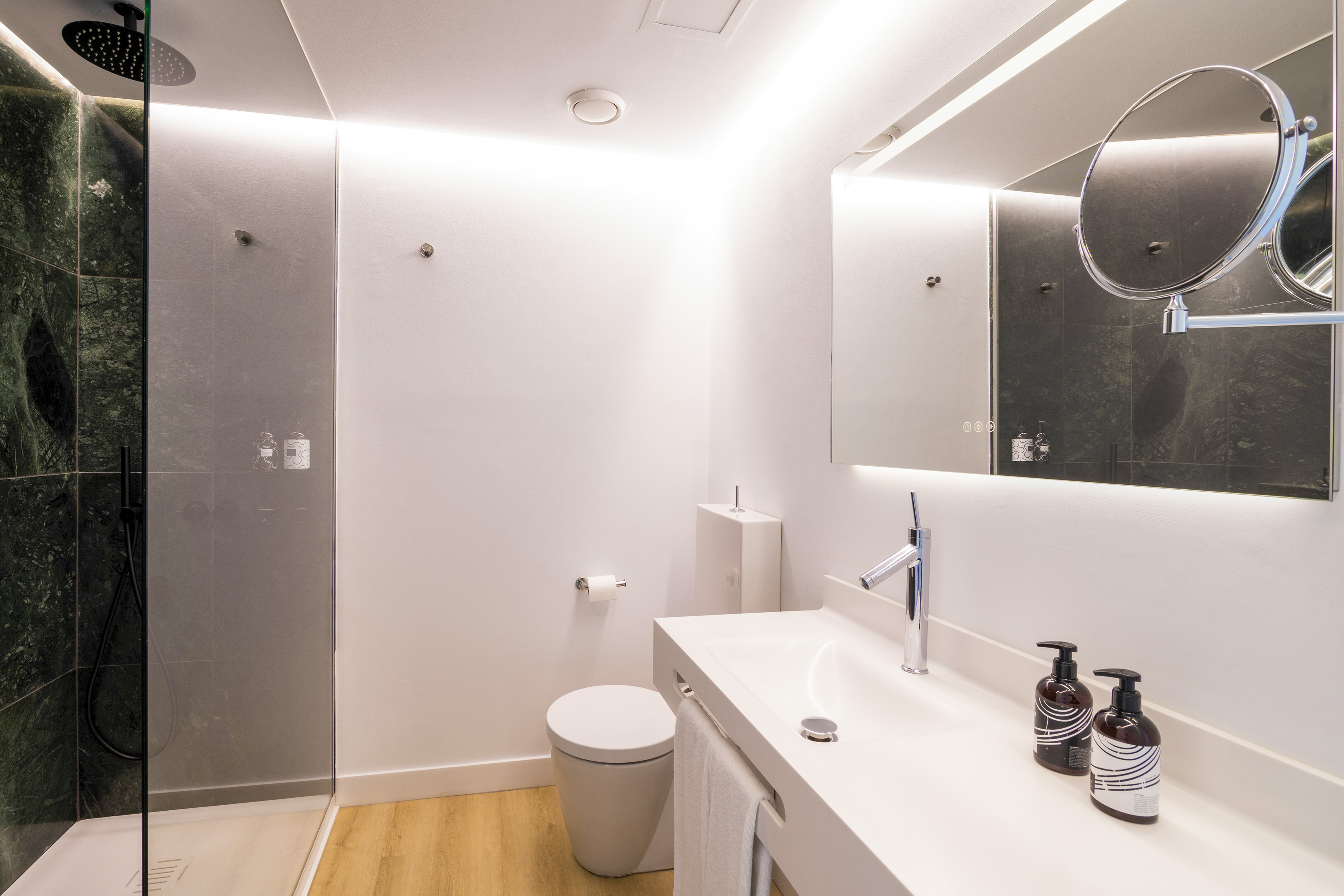 Modern bathroom with green marble shower, white vanity, toilet, and backlit mirror.