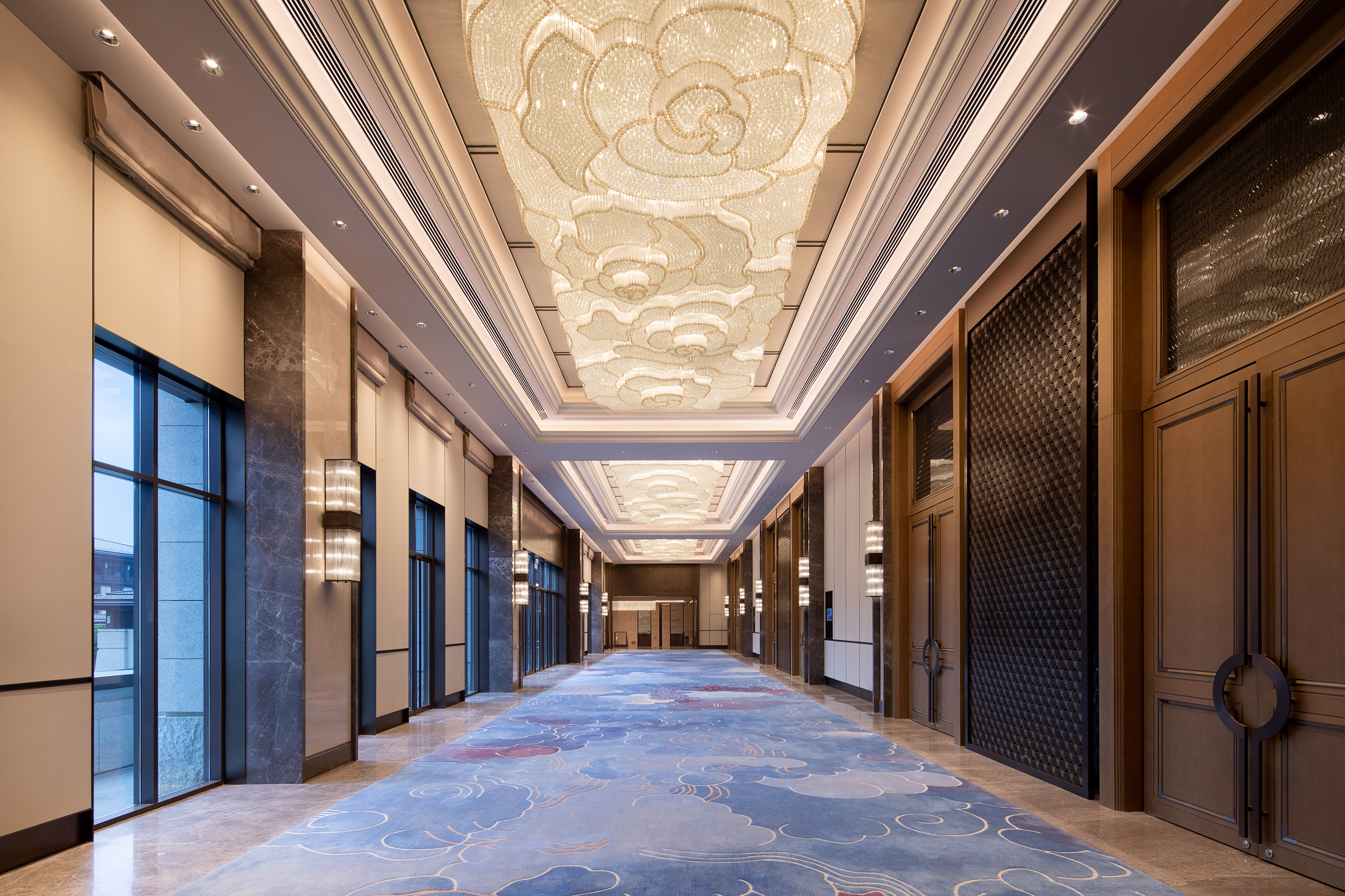 Luxury hallway with grand floral crystal chandeliers and blue cloud carpet.