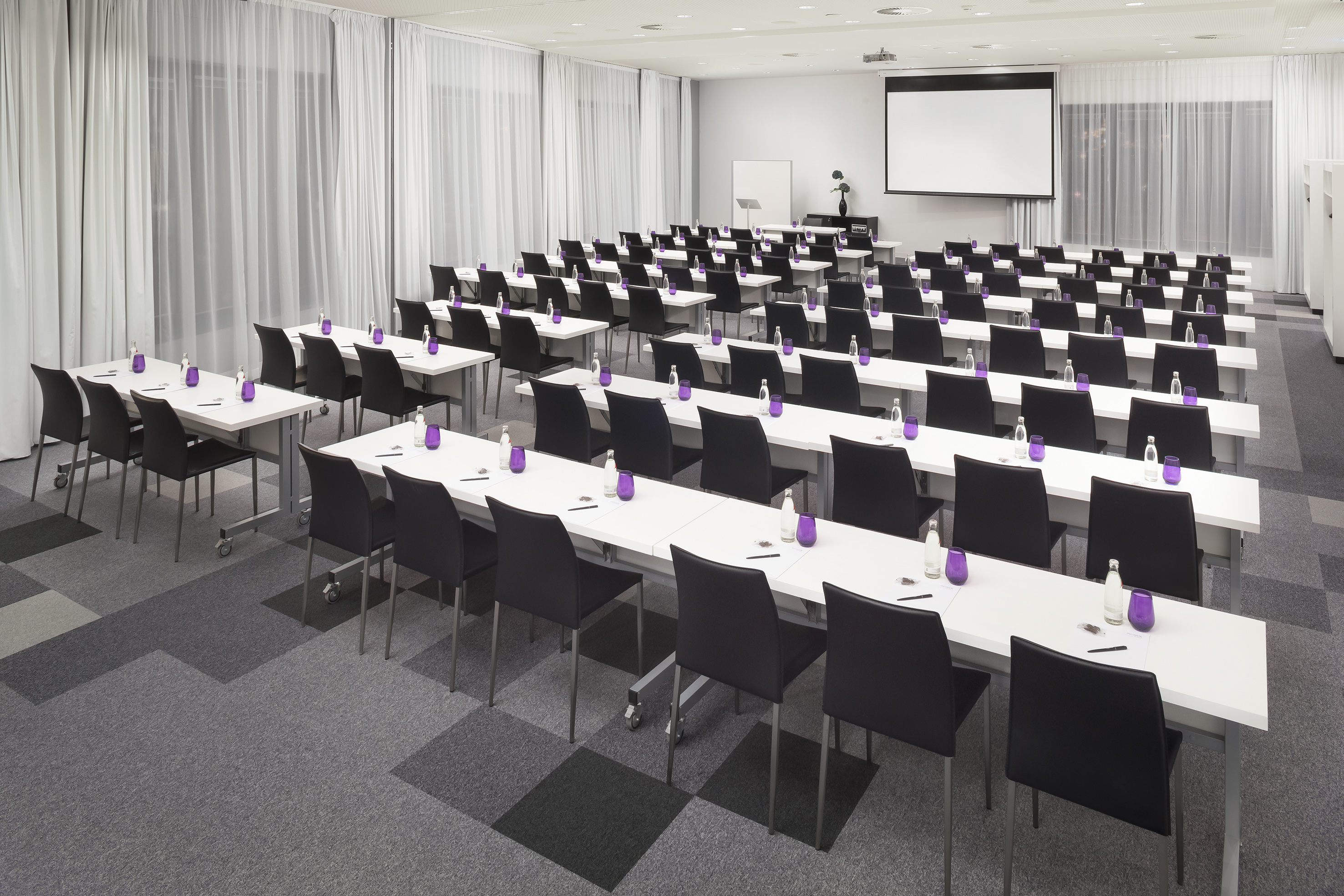 Modern conference room classroom setup with projector screen and water bottles.