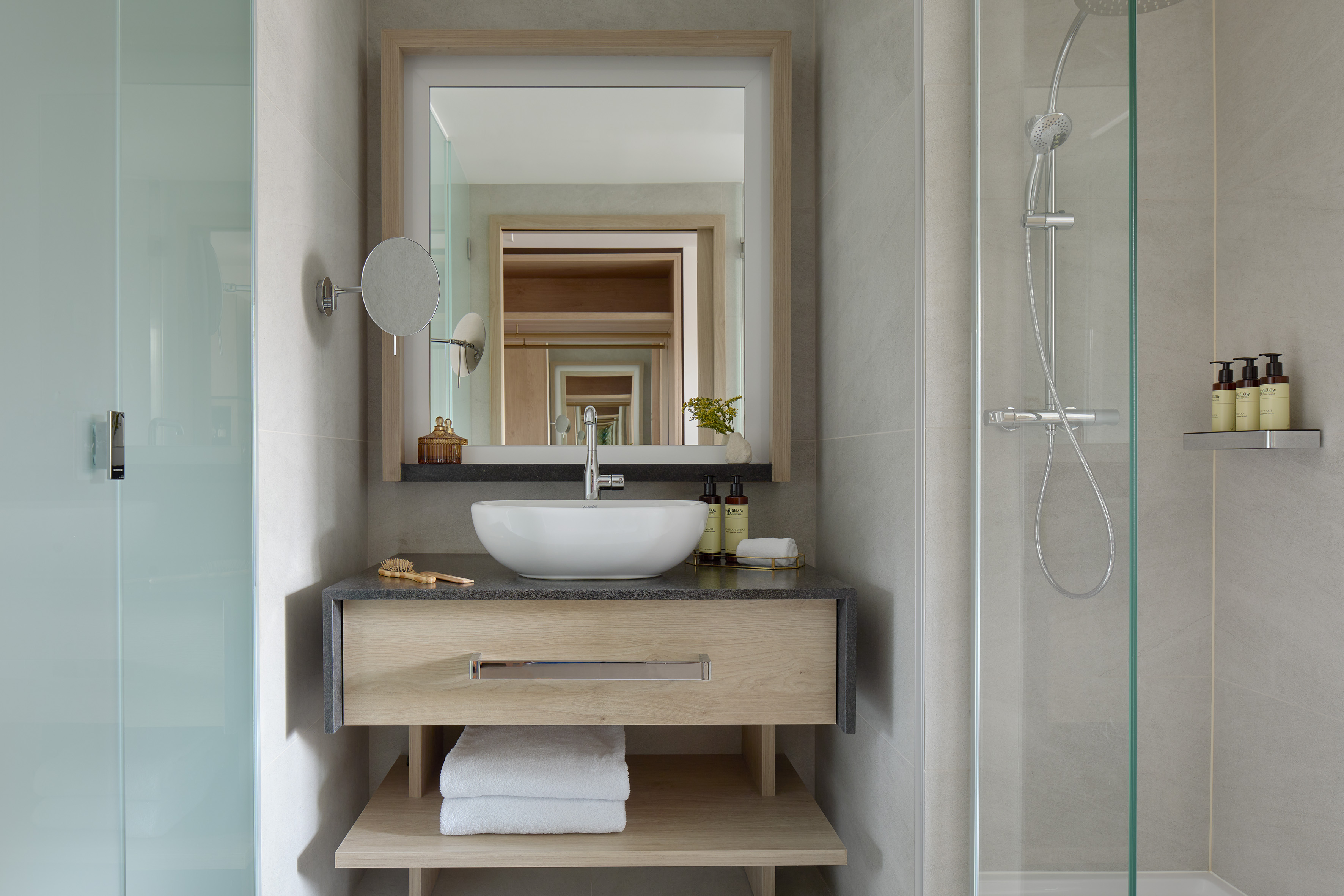 Modern hotel bathroom with wood vanity, vessel sink, mirror, and glass shower.