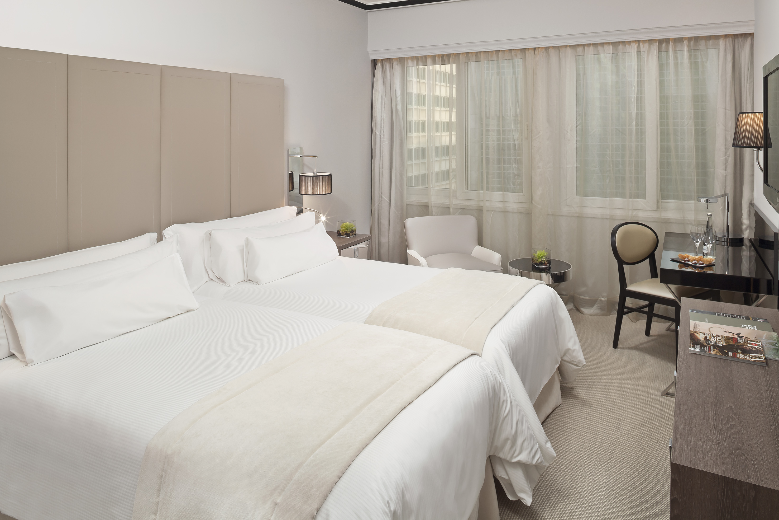 Hotel twin room with two beds, neutral decor, sheer window, and desk.