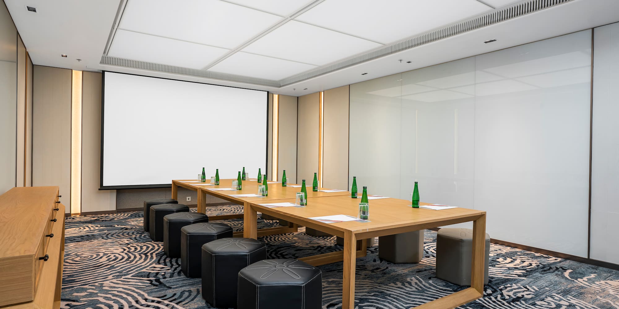 a table with green bottles on it and stools in a room with a projector screen