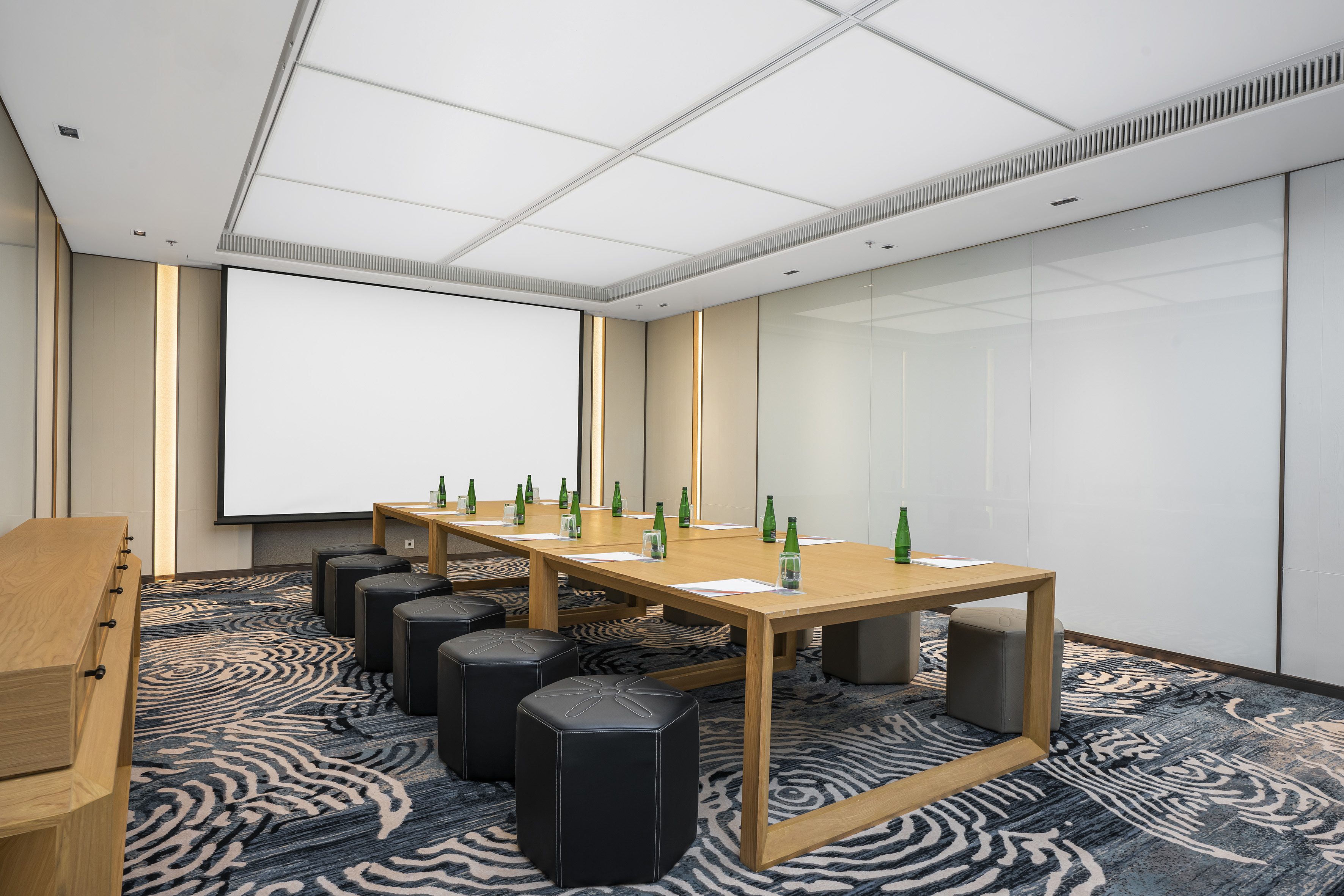 a table with green bottles on it and stools in a room with a projector screen