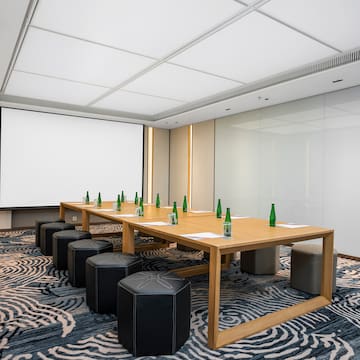a table with green bottles on it and stools in a room with a projector screen