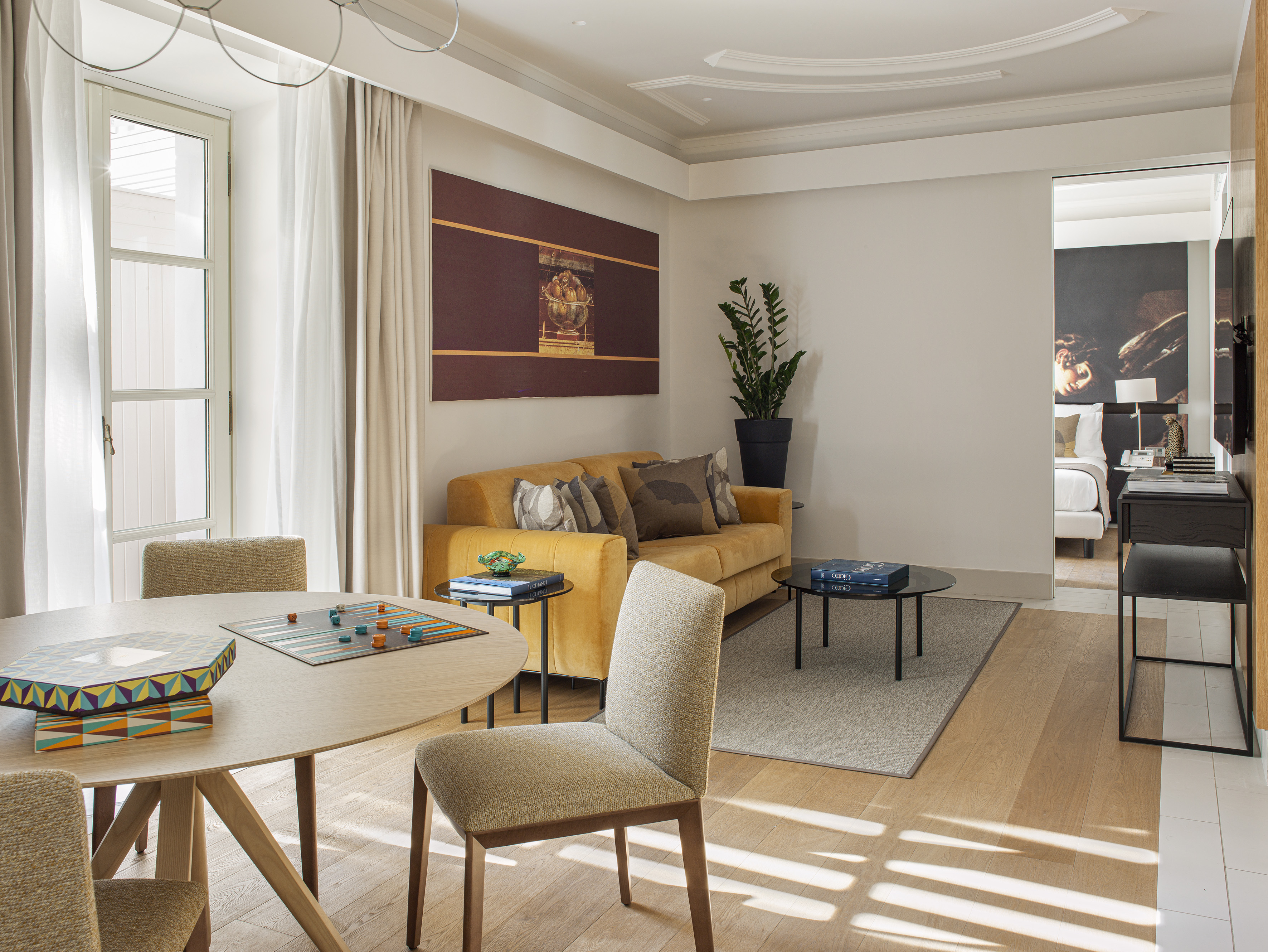 Sunny living area: yellow sofa, dining table with board games, hardwood floor.