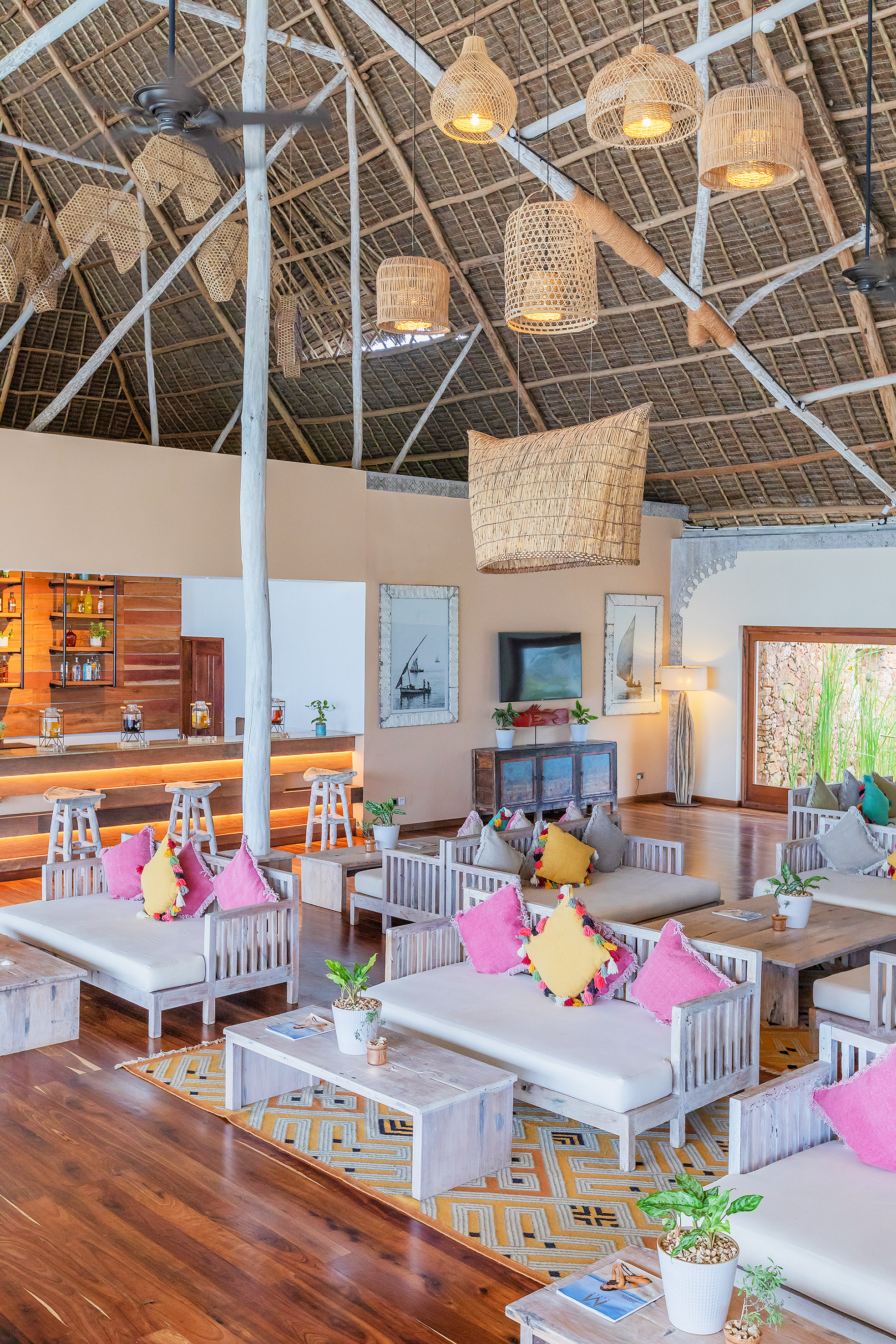 Tropical lounge with thatched roof, wicker lights, wooden sofas, and bar area.