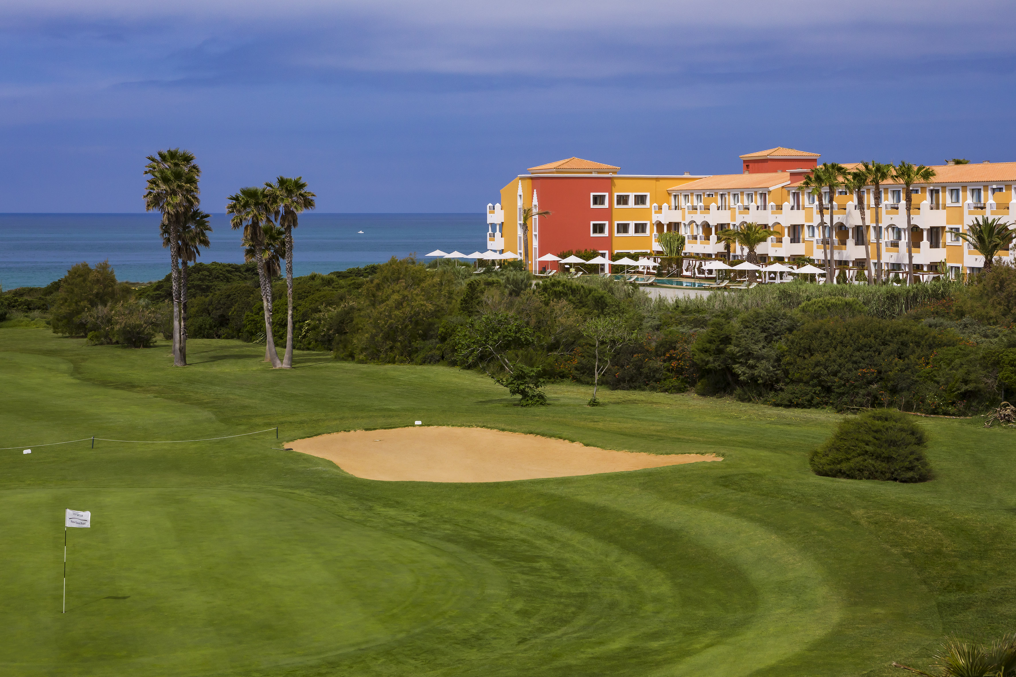 Oceanfront resort hotel and golf course with palm trees and sand trap.