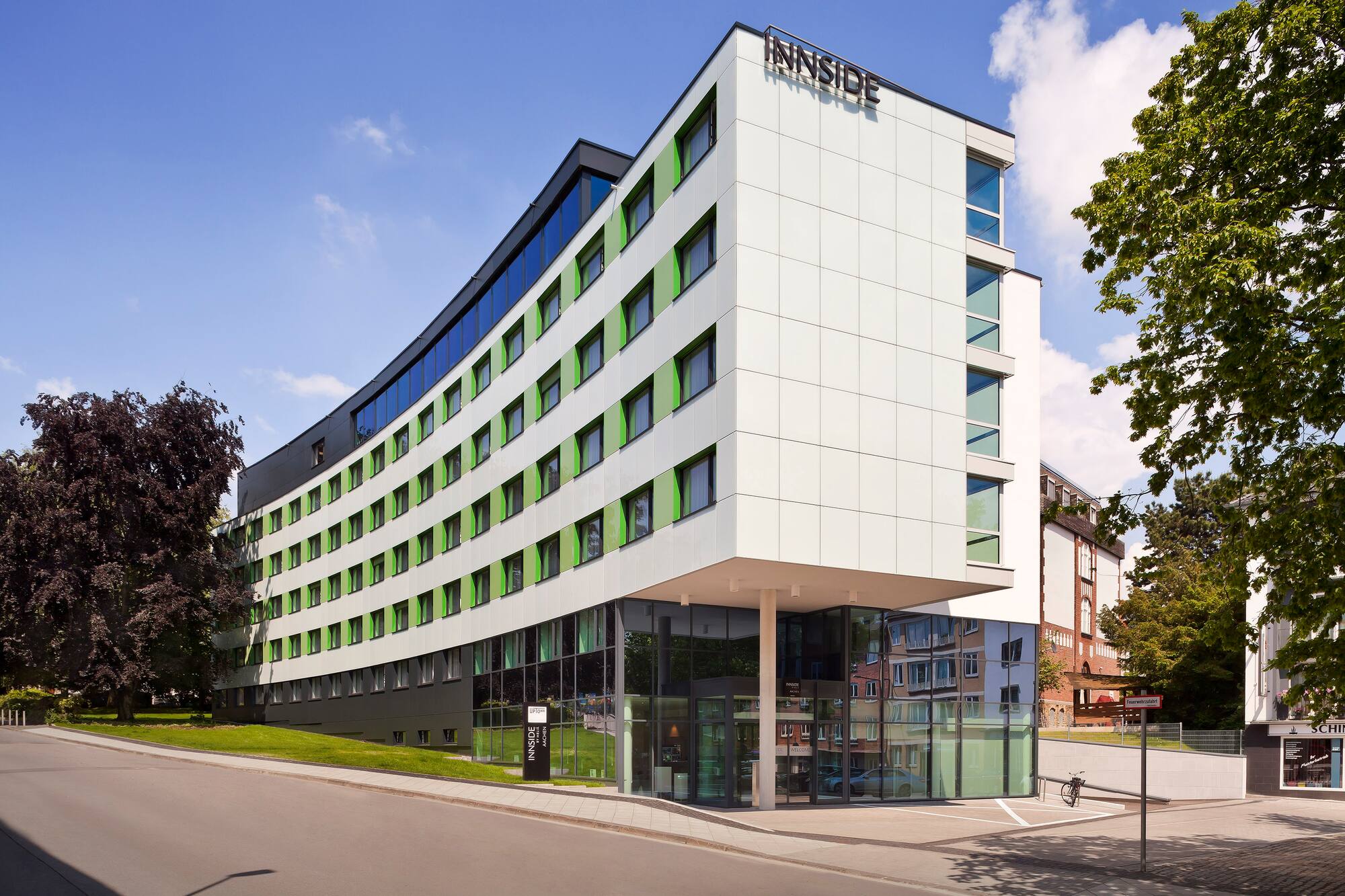 Curved Innside hotel building with white and green facade, glass entrance.