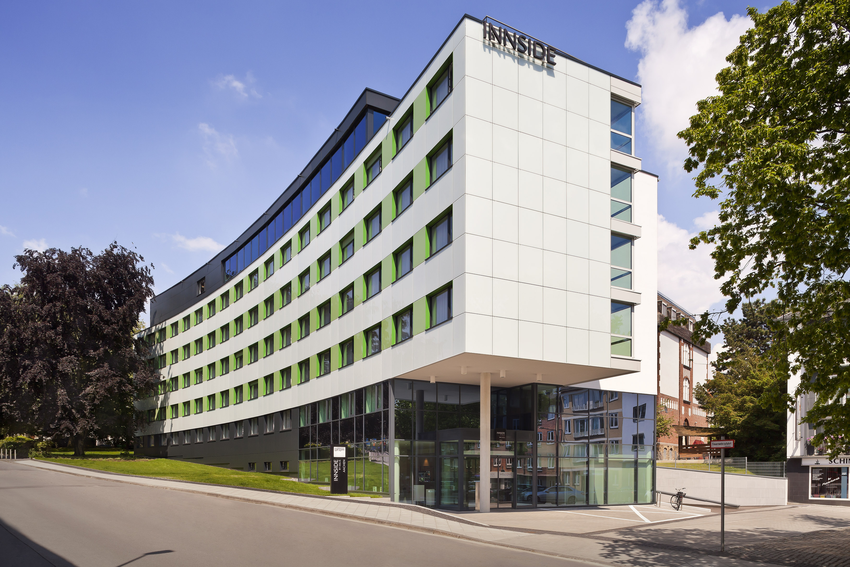 Curved Innside hotel building with white and green facade, glass entrance.