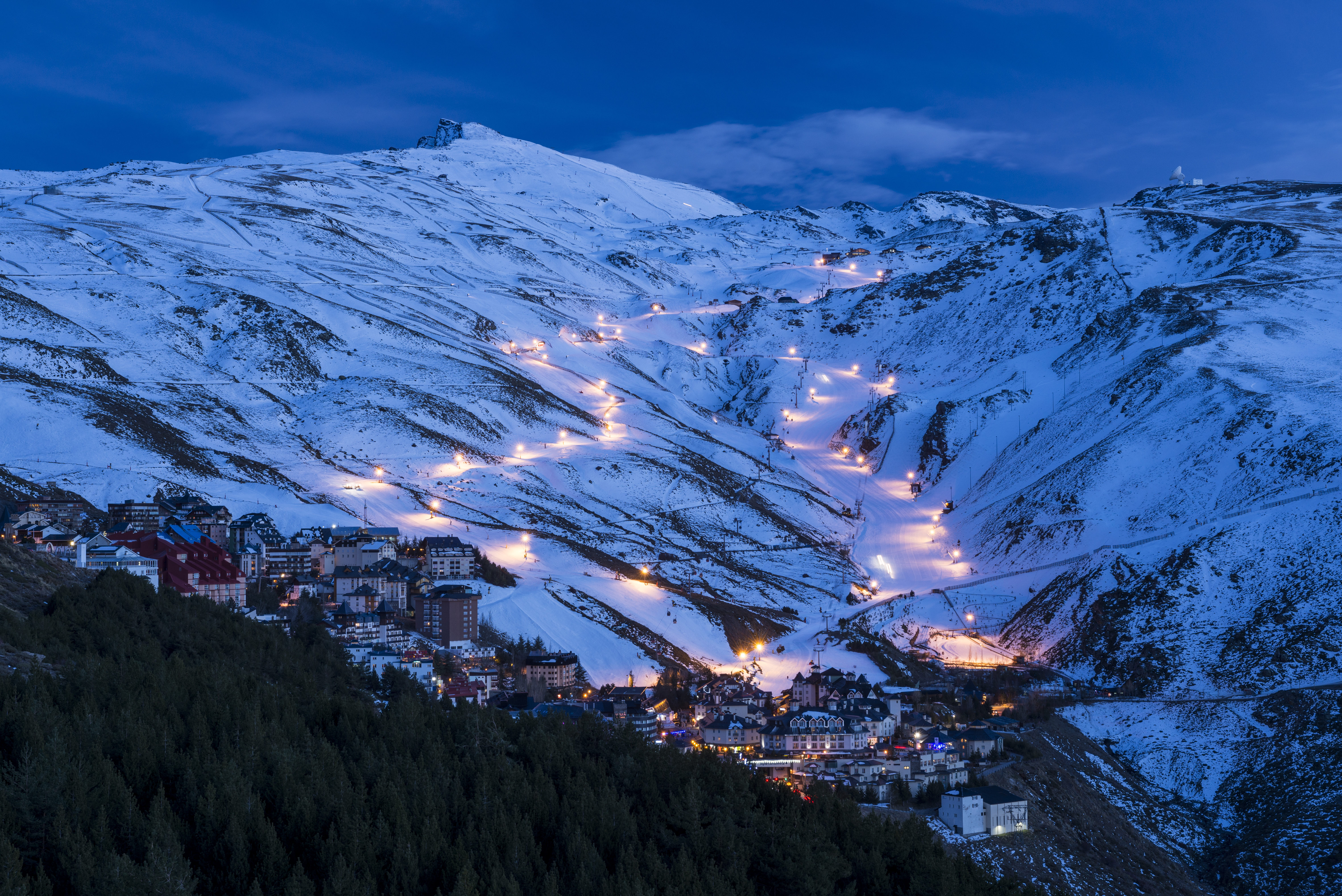 Illuminated ski resort town and glowing slopes on a snowy mountain at night.