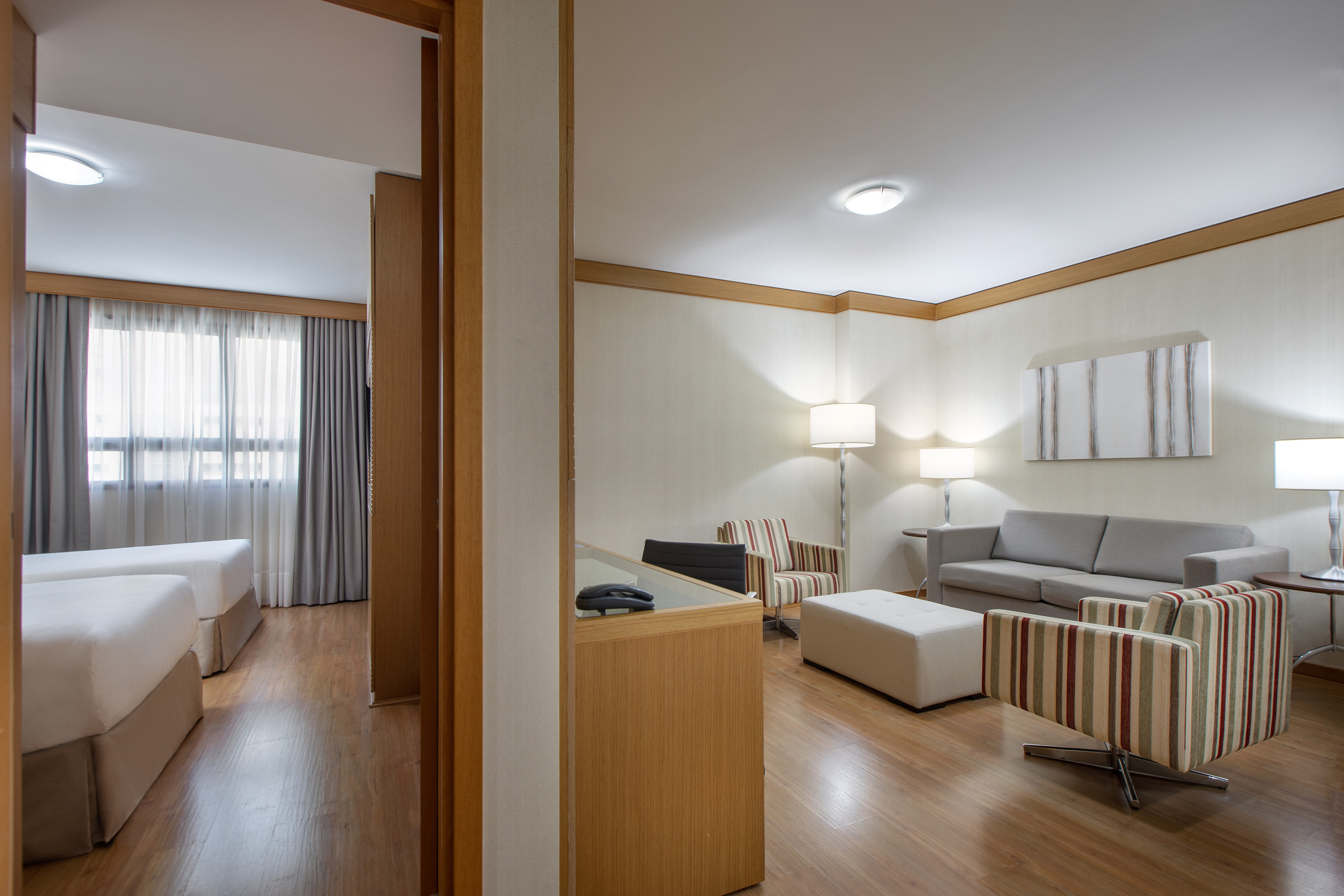 Modern hotel suite with living area, sofa, armchairs, and twin bedroom.