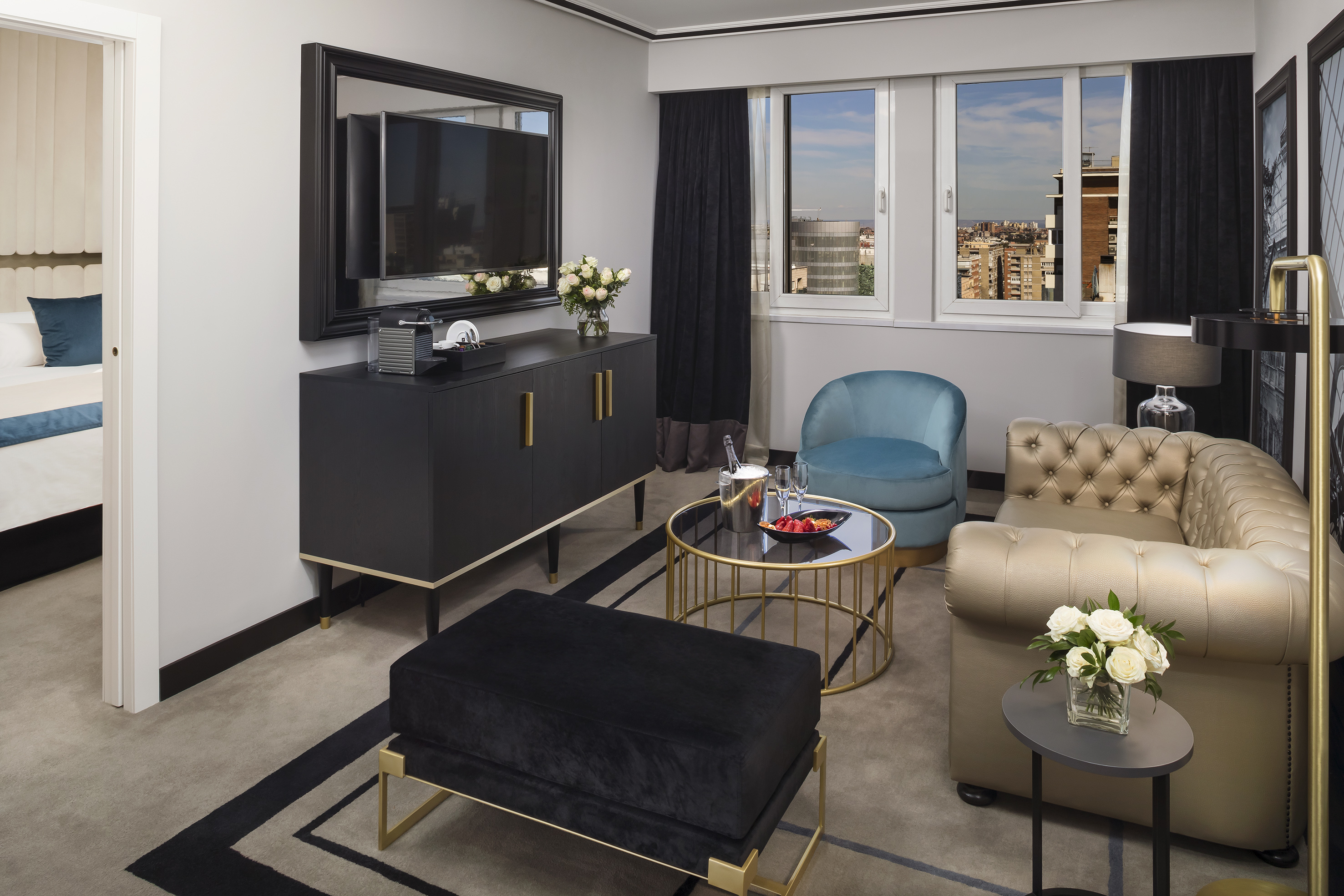 Elegant hotel suite living room with tufted sofa, armchair, TV, and city view.