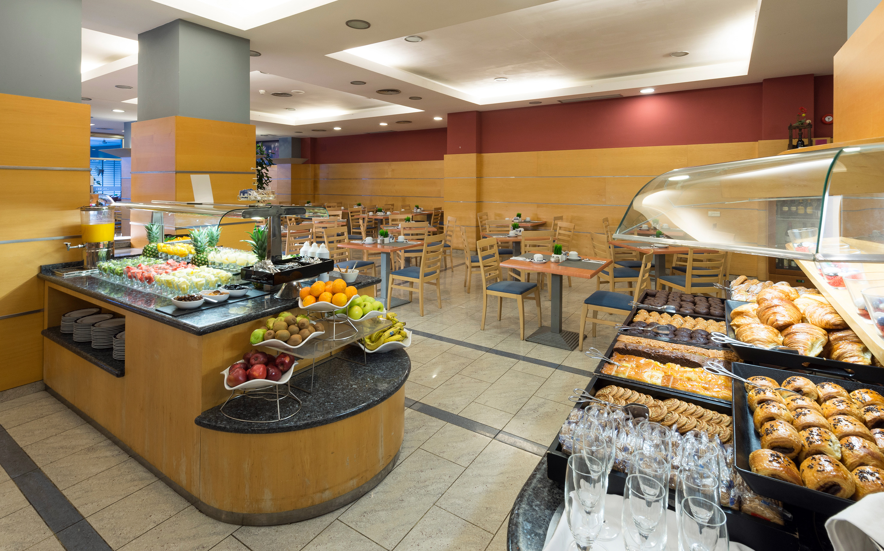 Hotel breakfast buffet with fresh fruit, pastries, and dining tables.