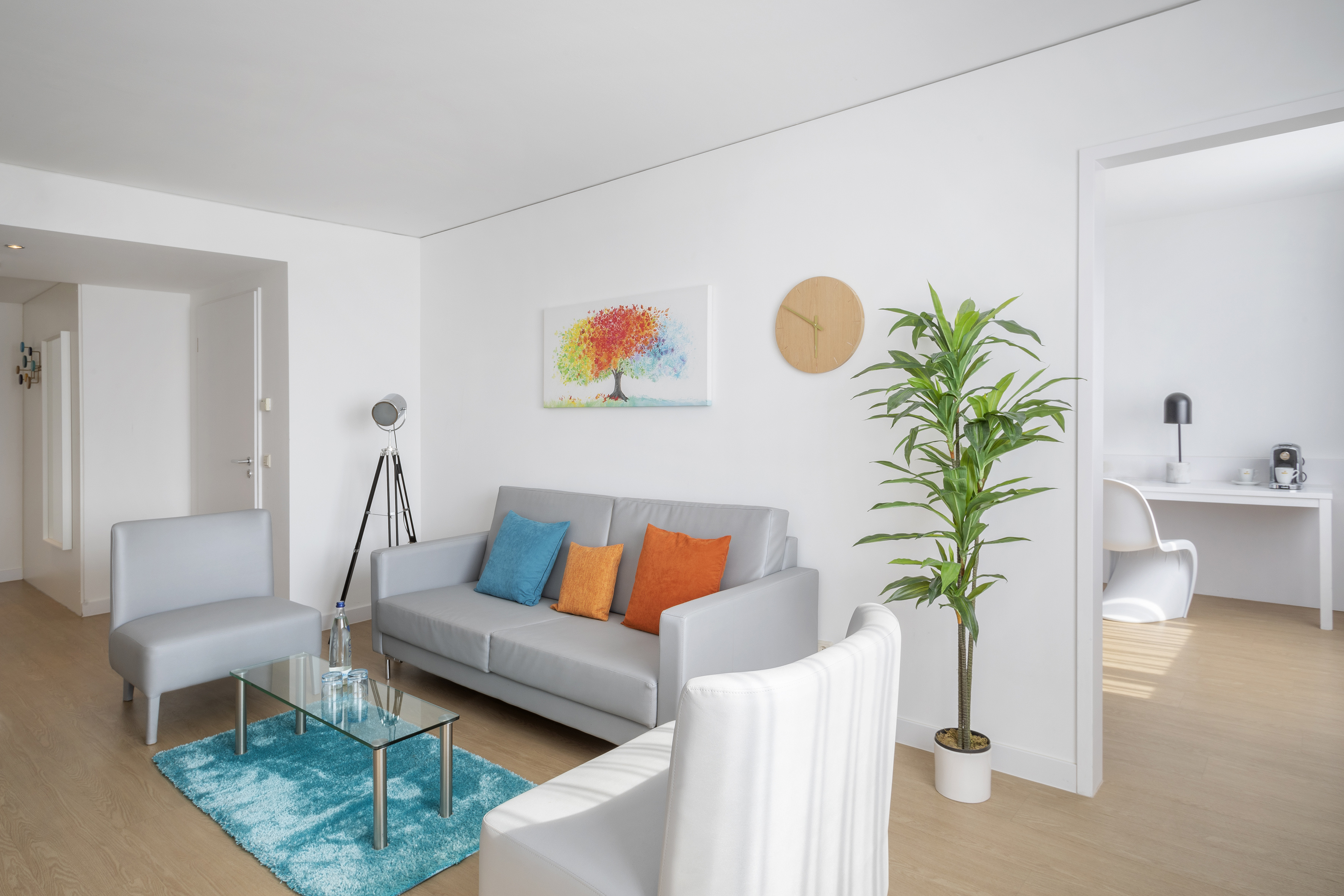 Bright modern living room with grey sofa, colorful painting, blue rug.
