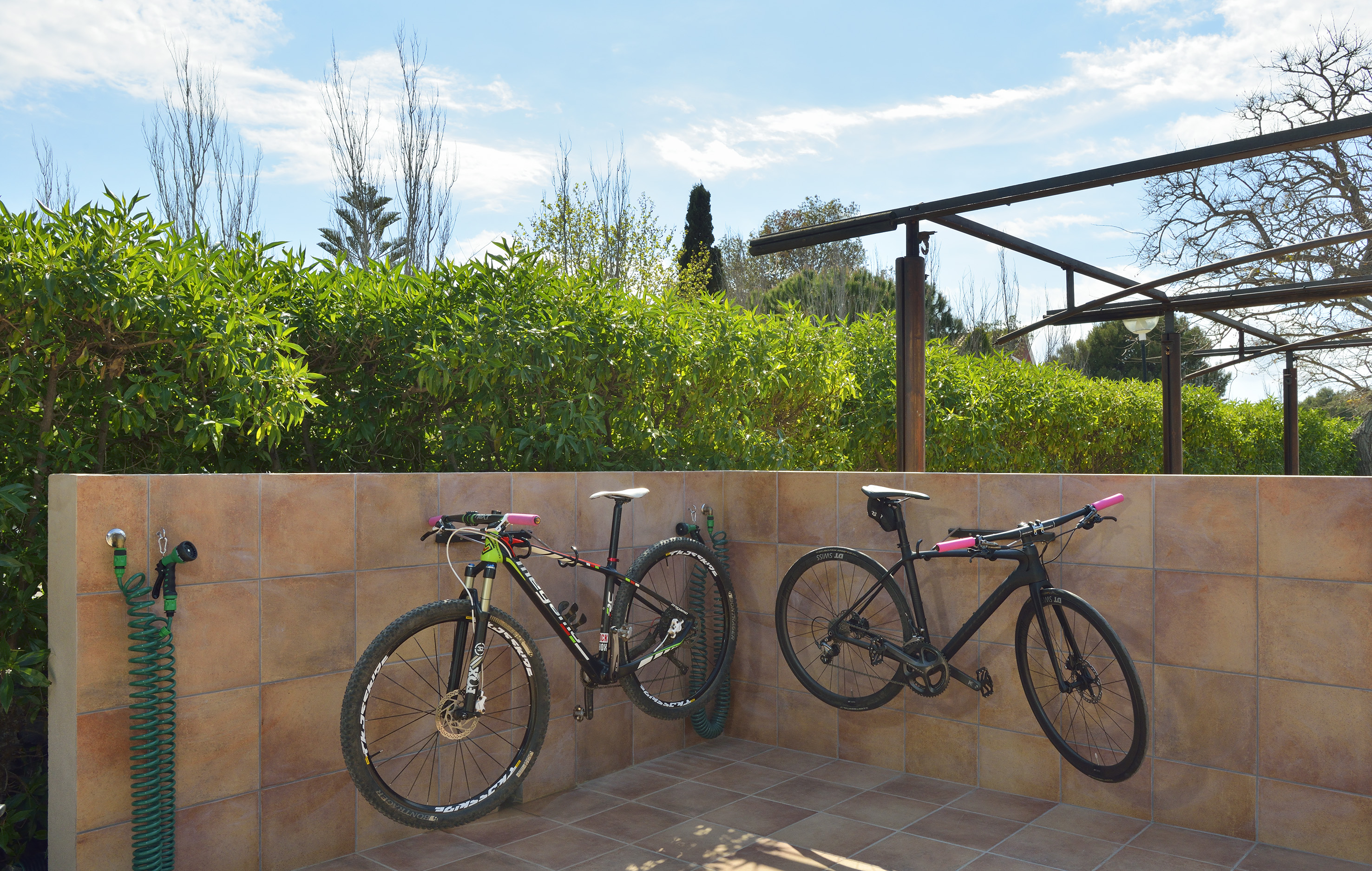 Outdoor bike wash station with two bicycles mounted on a tiled wall.