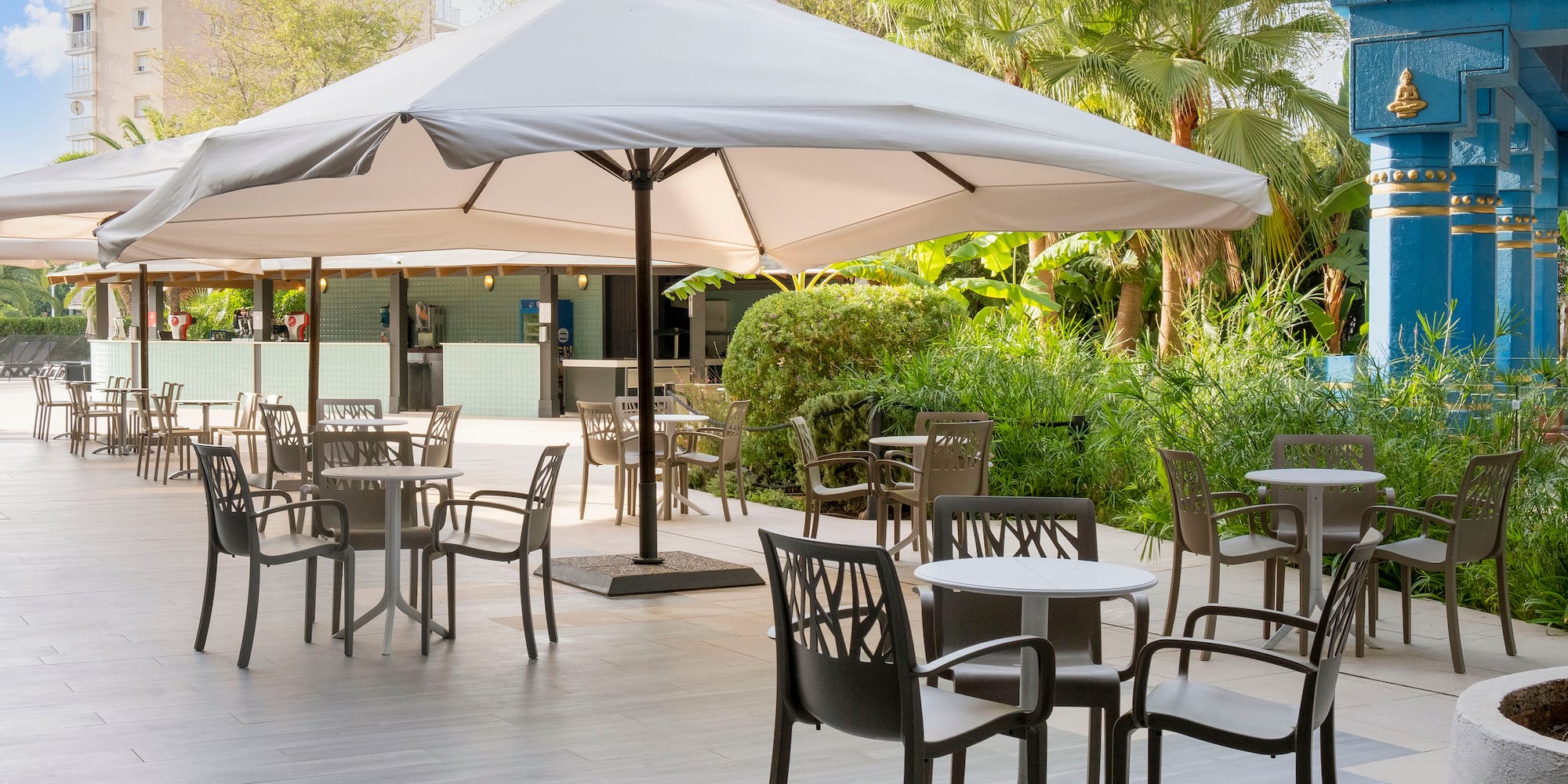 a patio with tables and chairs under a large umbrella