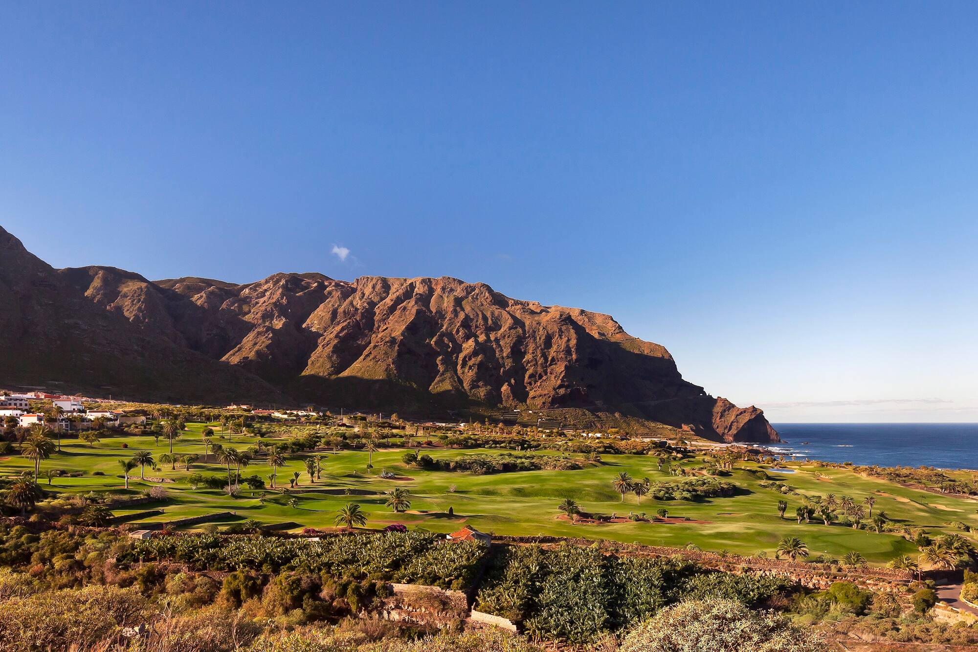 Coastal golf course resort with mountains, ocean, and palm trees.