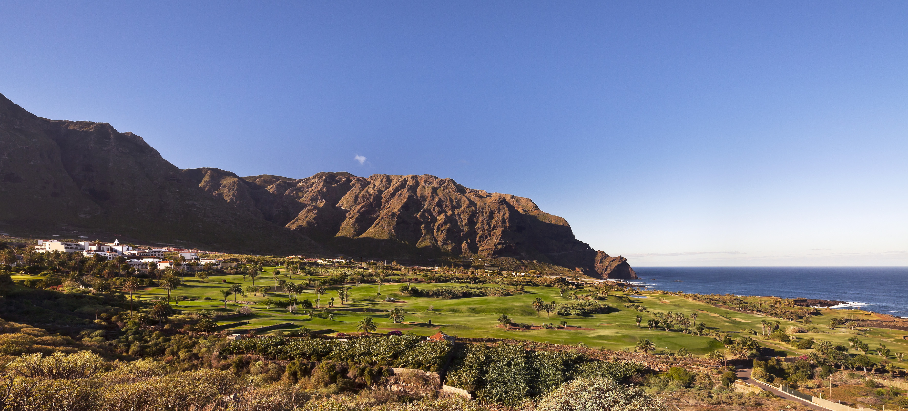 Coastal golf course resort with mountains, ocean, and palm trees.